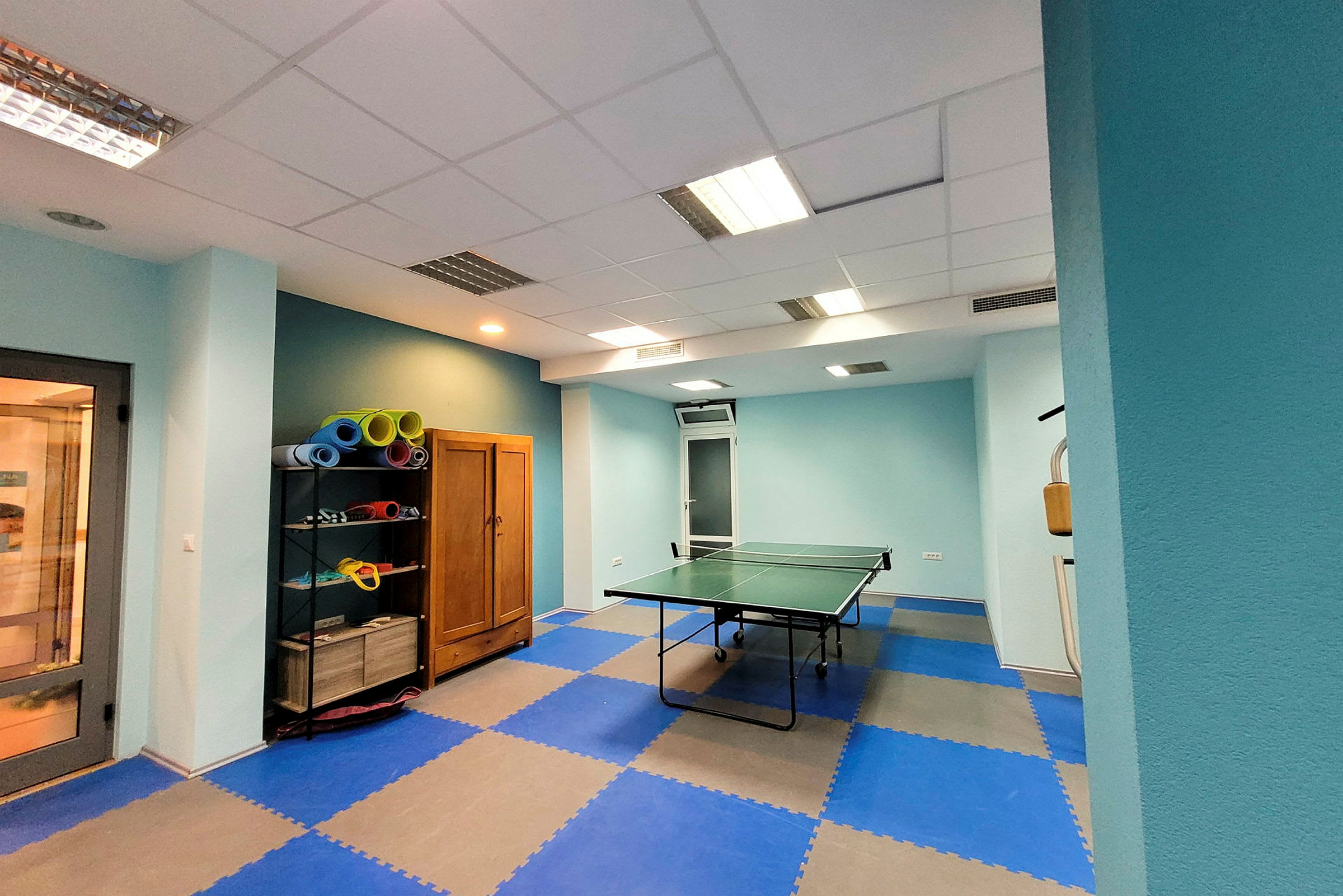 Et billede af et rum med bordtennisbord og hylde med yogamåtter. (AI-genereret tekst)