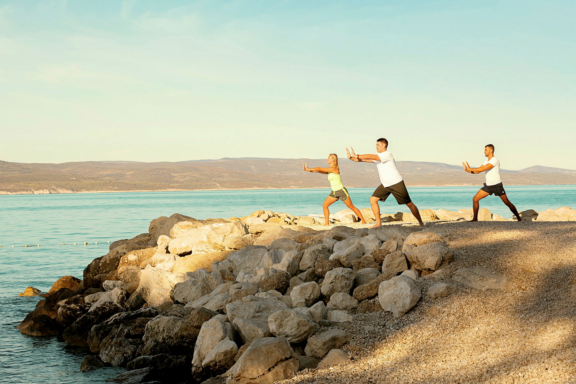 Tre personer laver tai chi på stranden nær havet. (AI-genereret tekst)