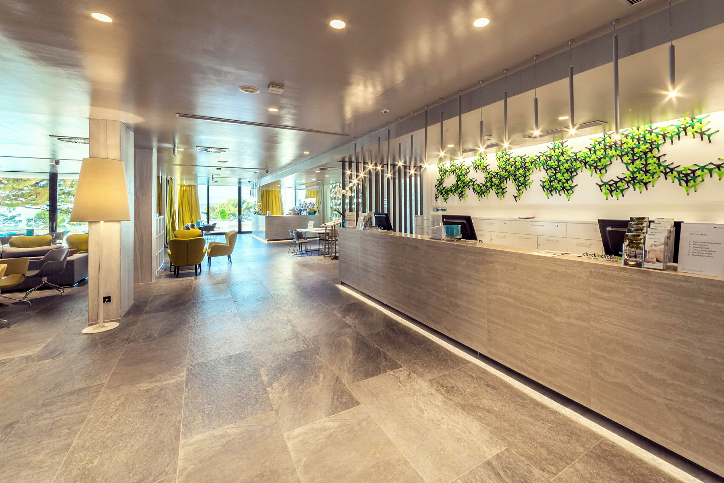 Receptionen på et moderne hotel med siddepladser, store vinduer og en dekoreret væg. (AI-genereret tekst)
