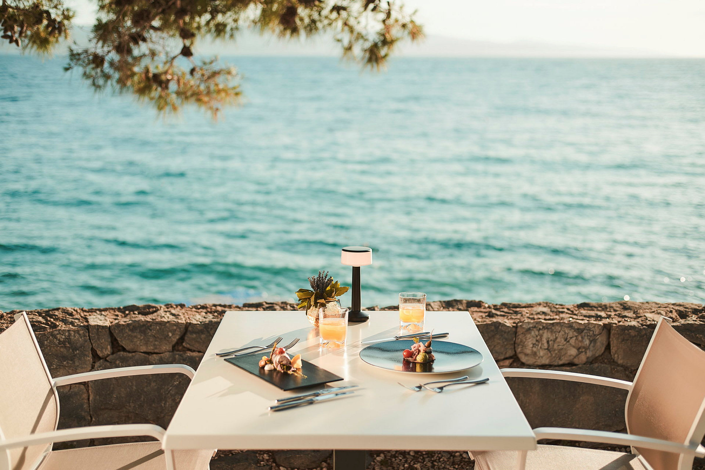 To serverede tallerkener og drikkevarer på et bord ved havet. (AI-genereret tekst)