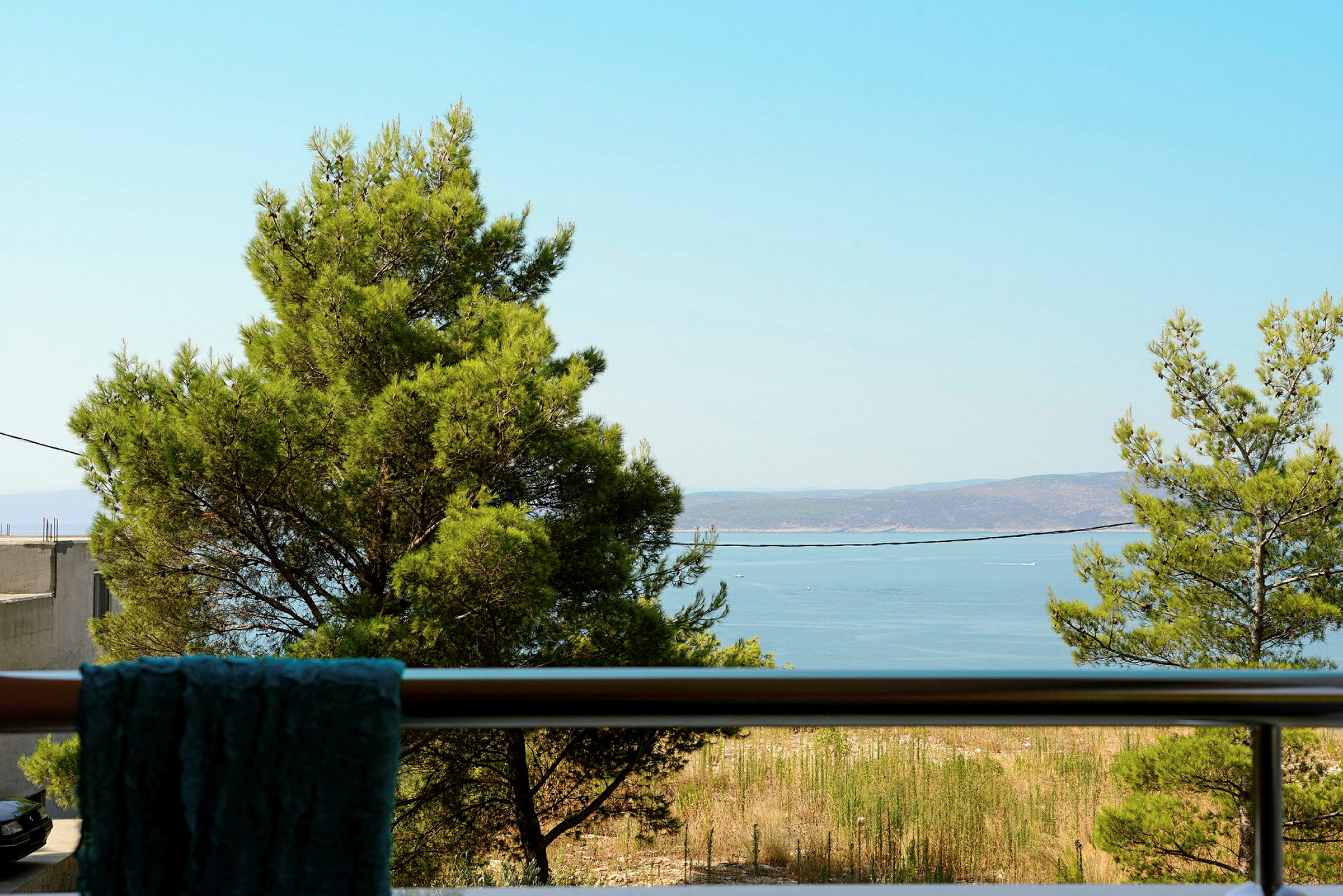 Udsigt fra en balkon med træer og havet i baggrunden. (AI-genereret tekst)