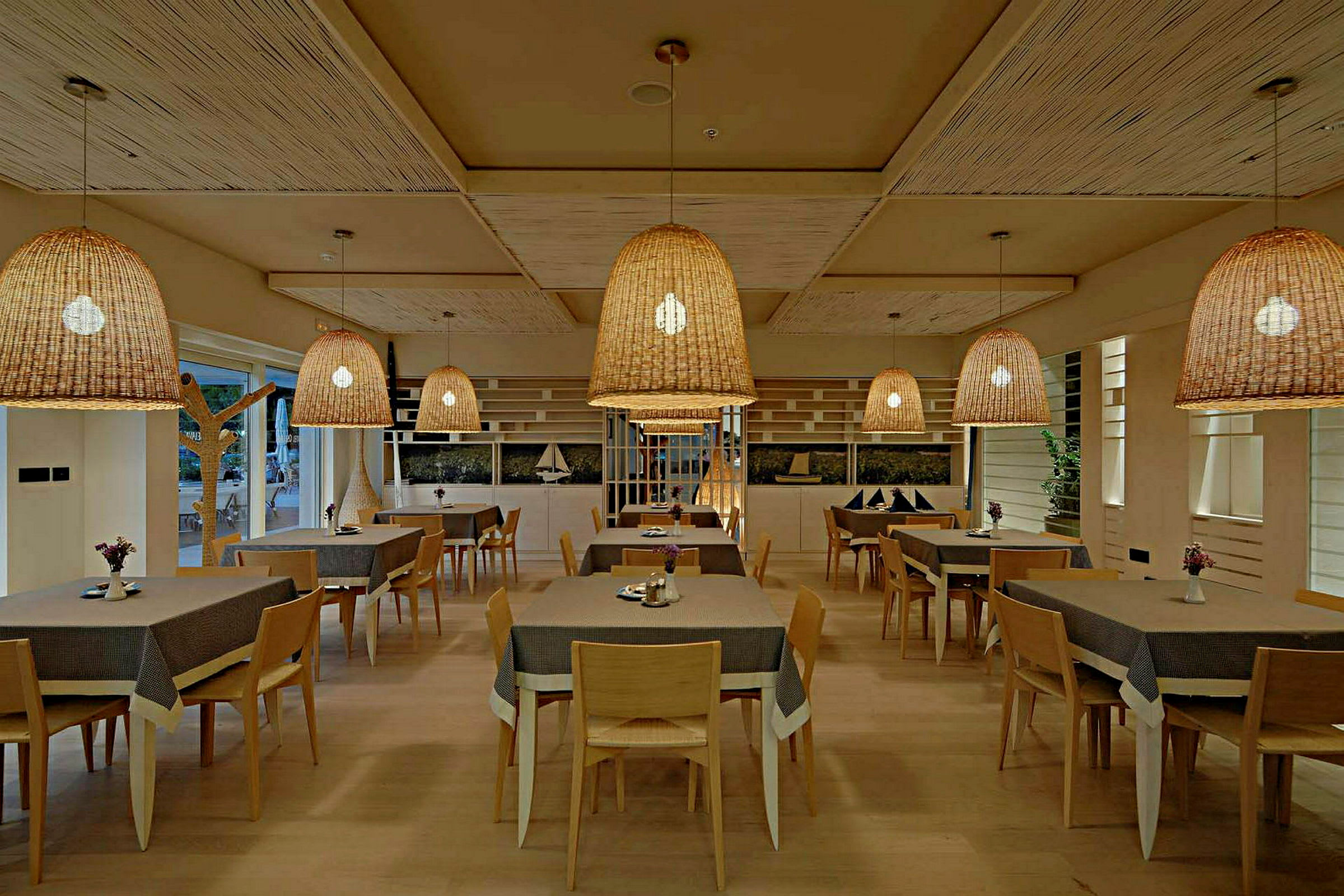 En restaurant med flere borde og stole samt store flettede loftslamper. (AI-genereret tekst)