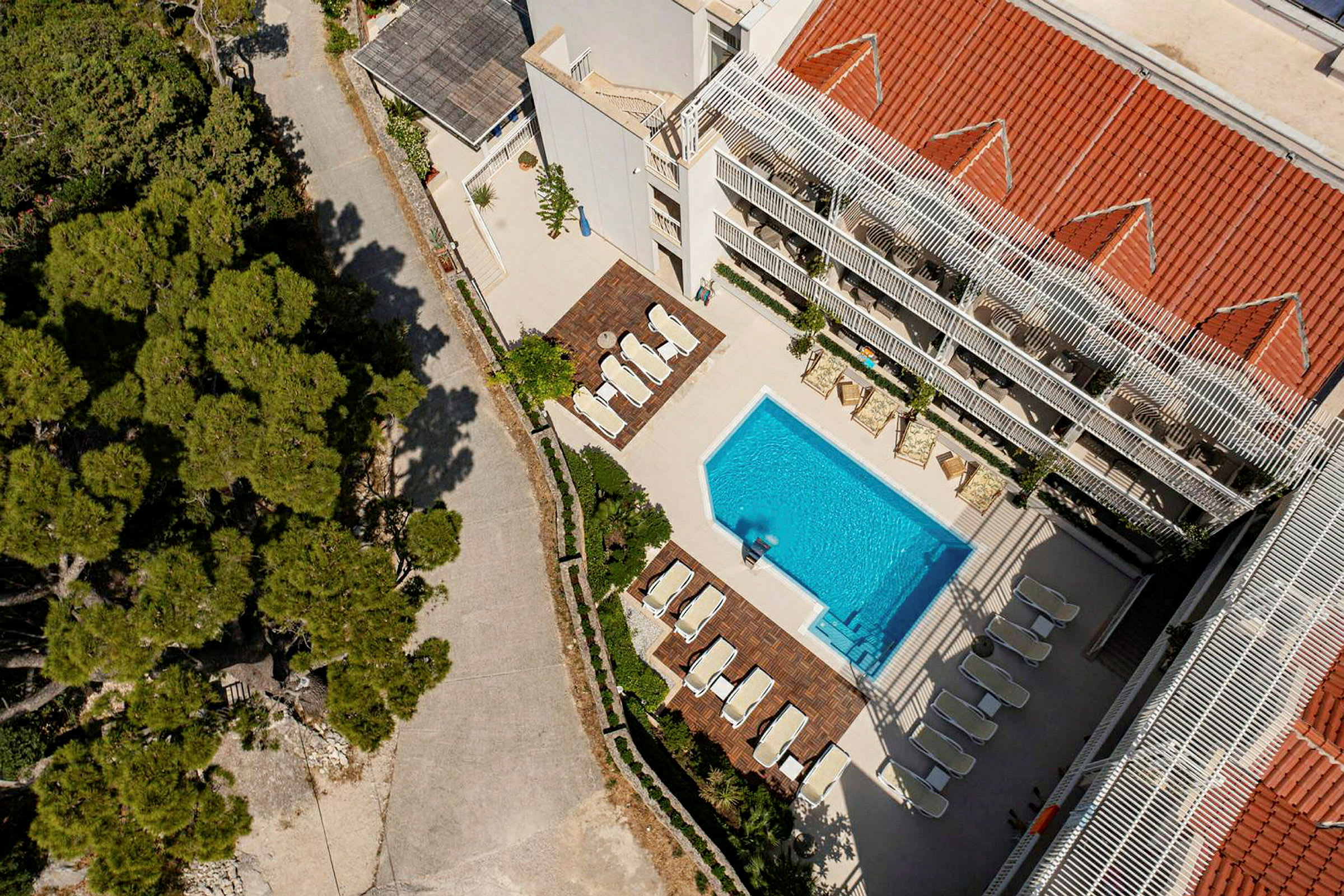Luftfoto af en bygning med swimmingpool og liggestole, omgivet af træer. (AI-genereret tekst)
