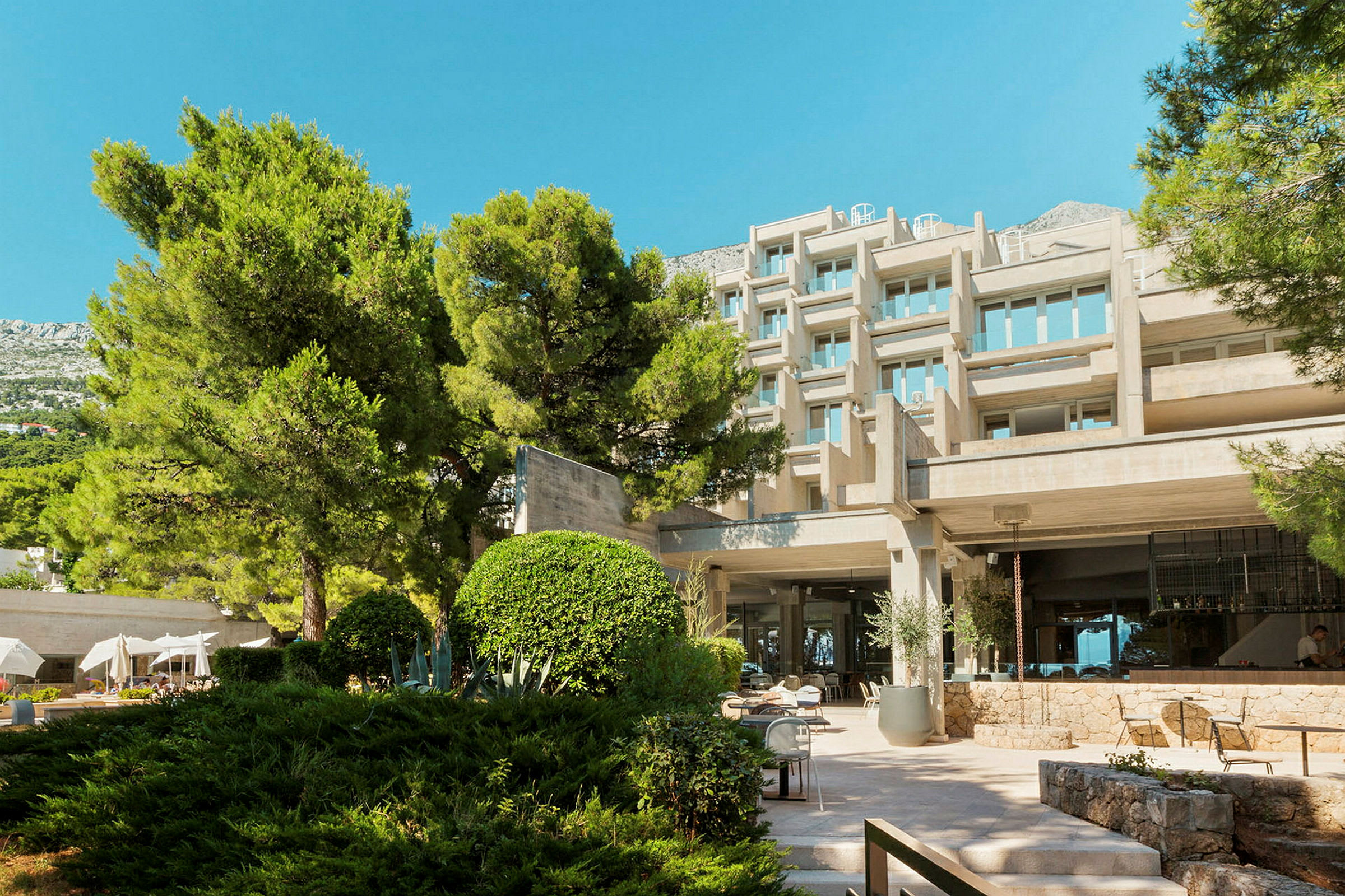 Et moderne hotel omgivet af beplantning og med en stenbelagt gårdhave. (AI-genereret tekst)