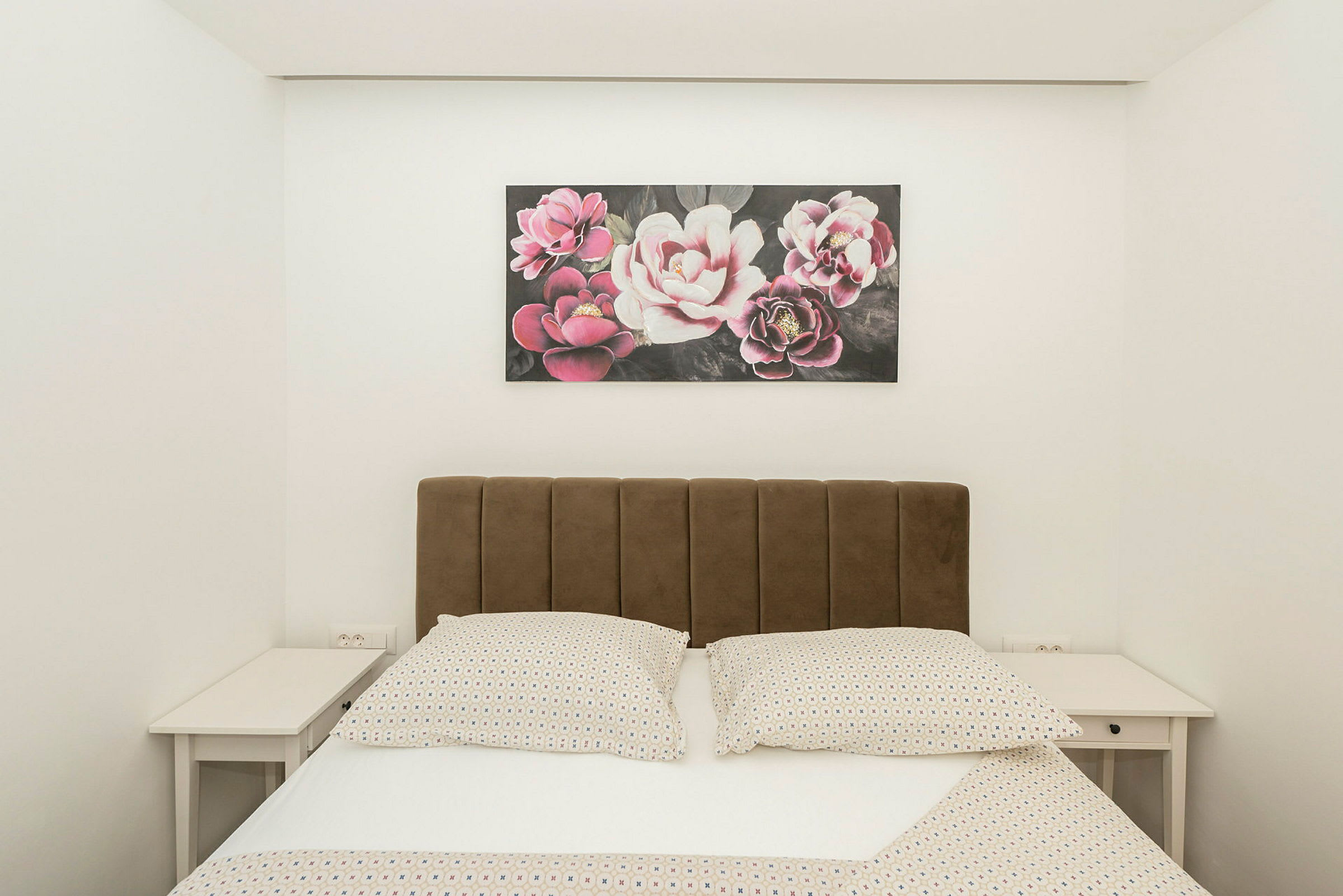 Seng med brun sengegavl, to natborde og et maleri med blomstermotiv ovenover. (AI-genereret tekst)