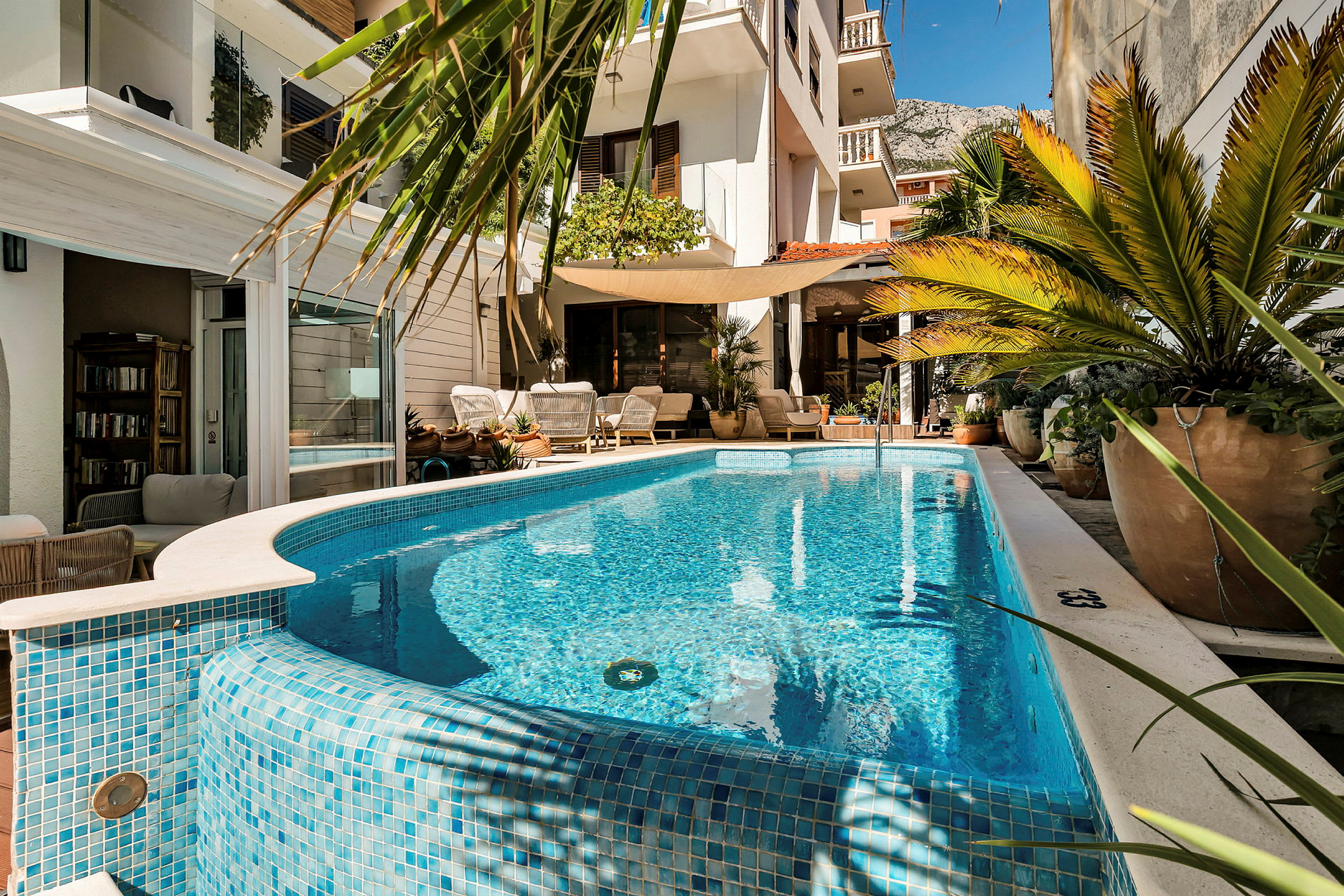 Udendørs pool ved en indbydende terrasse med planter og siddepladser. (AI-genereret tekst)