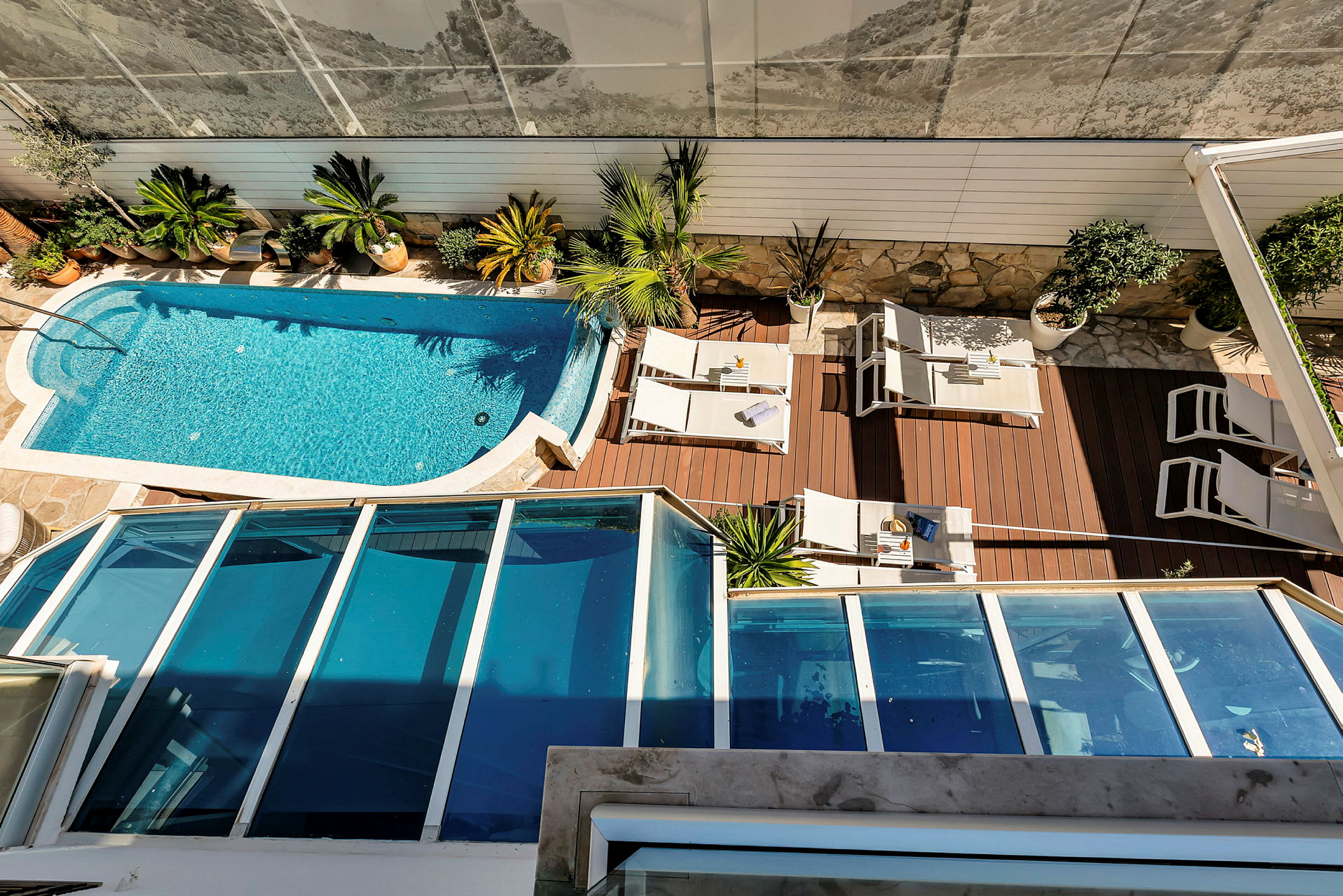 En pool og en terrasse med liggestole og borde, omgivet af planter. (AI-genereret tekst)