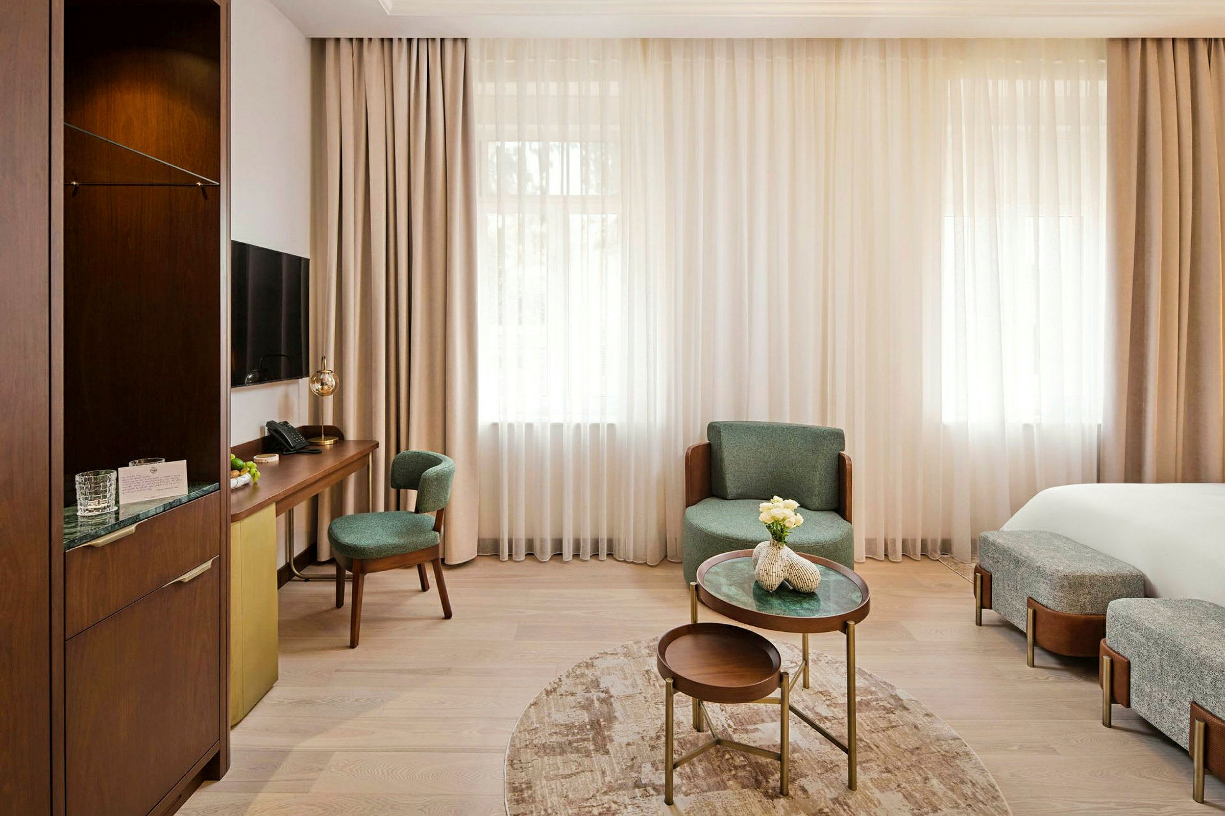 Et lyst hotelværelse med moderne møbler, et skrivebord med stole og et lille sofabord med dekorative blomster. (AI-genereret tekst)