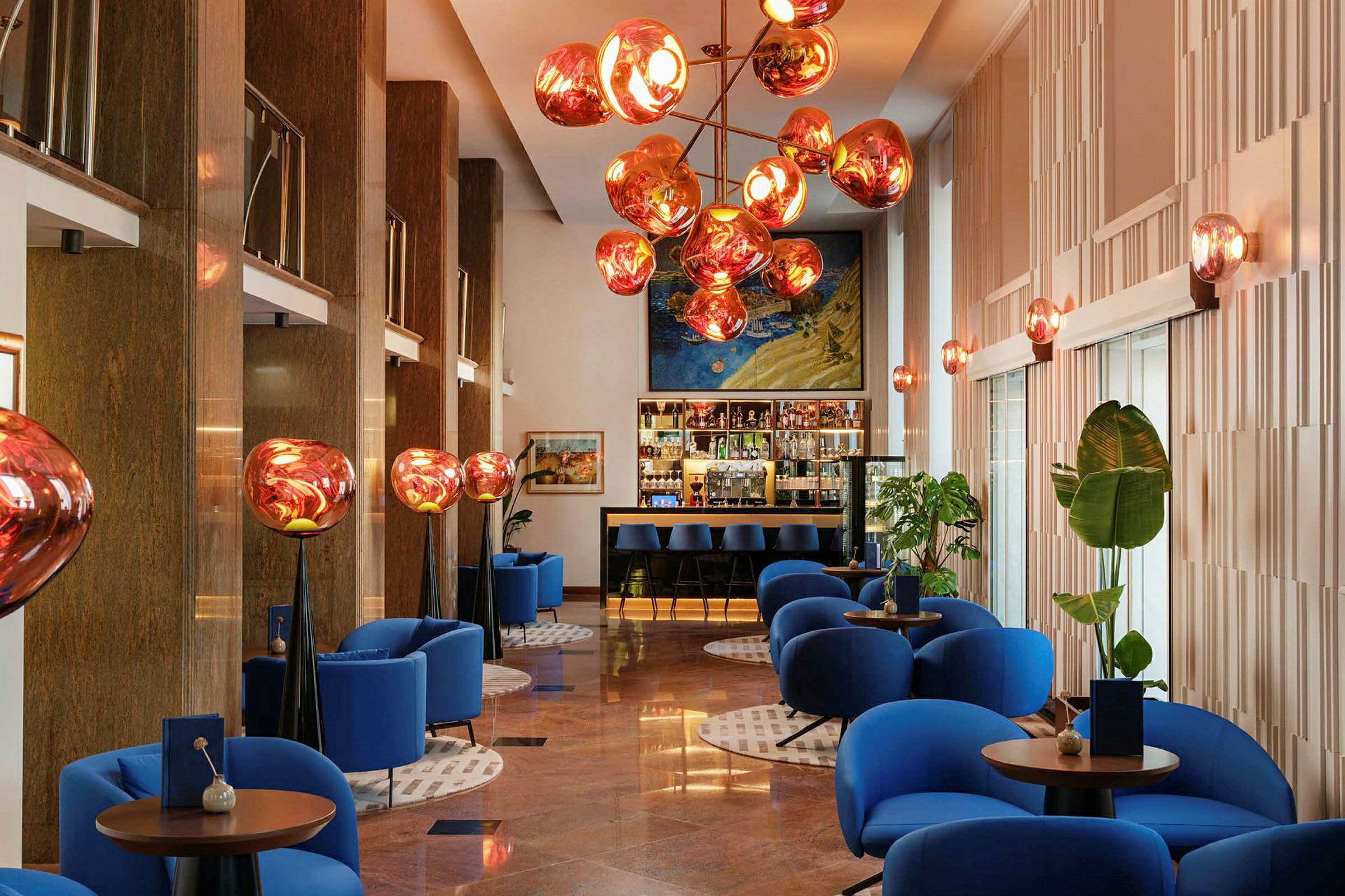 En moderne hotel-lobby med blå lænestole, runde borde og dekorativ loftbelysning. (AI-genereret tekst)