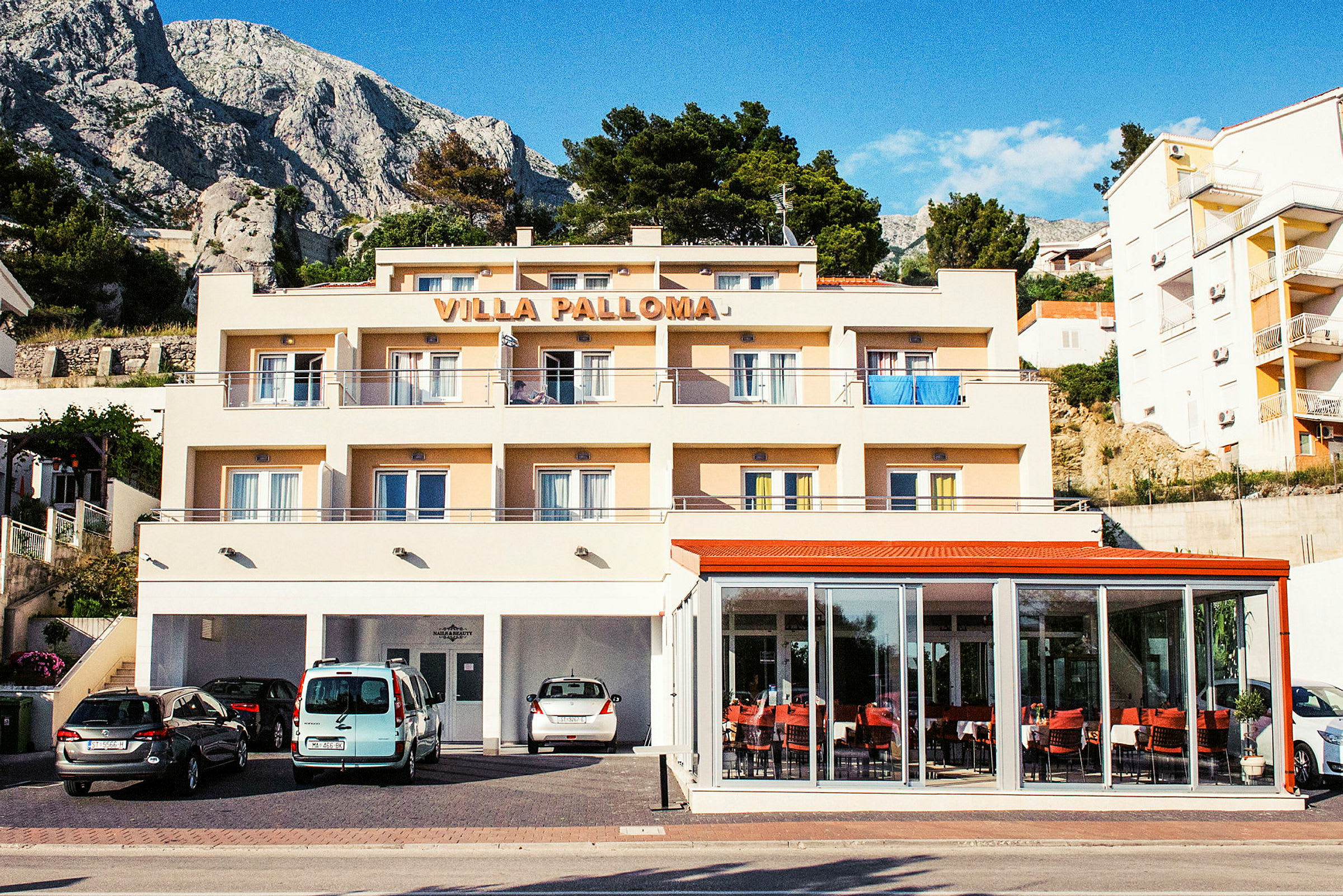 En bygning med teksten 'Villa Palloma' øverst, med altaner og parkerede biler foran. (AI-genereret tekst)