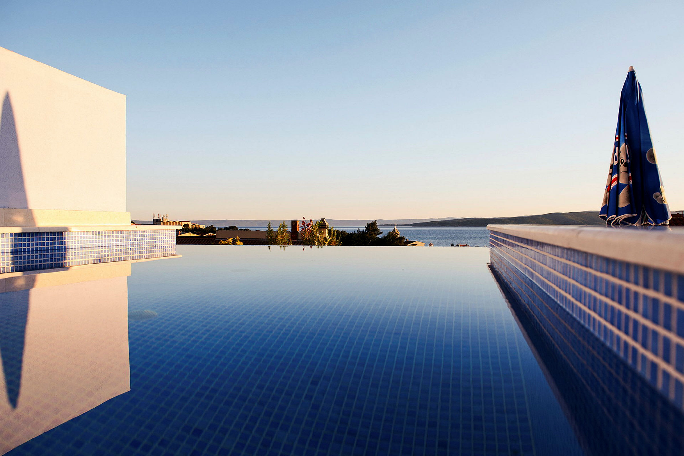 Udsigt over en pool med klar himmel og baggrund af hav og bakker. (AI-genereret tekst)