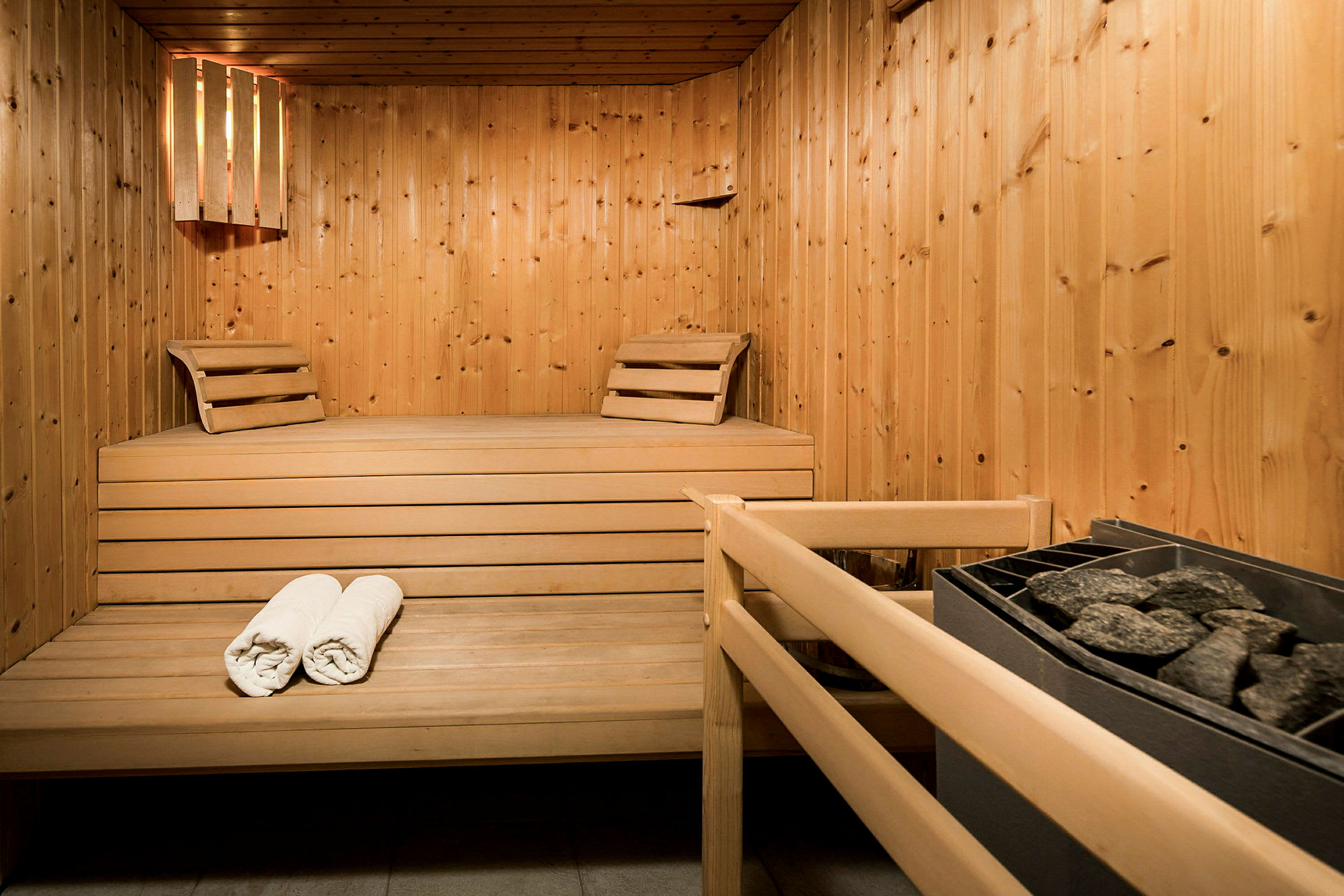 Billede af en sauna med træinteriør, to håndklæder og en ovn med saunasten. (AI-genereret tekst)