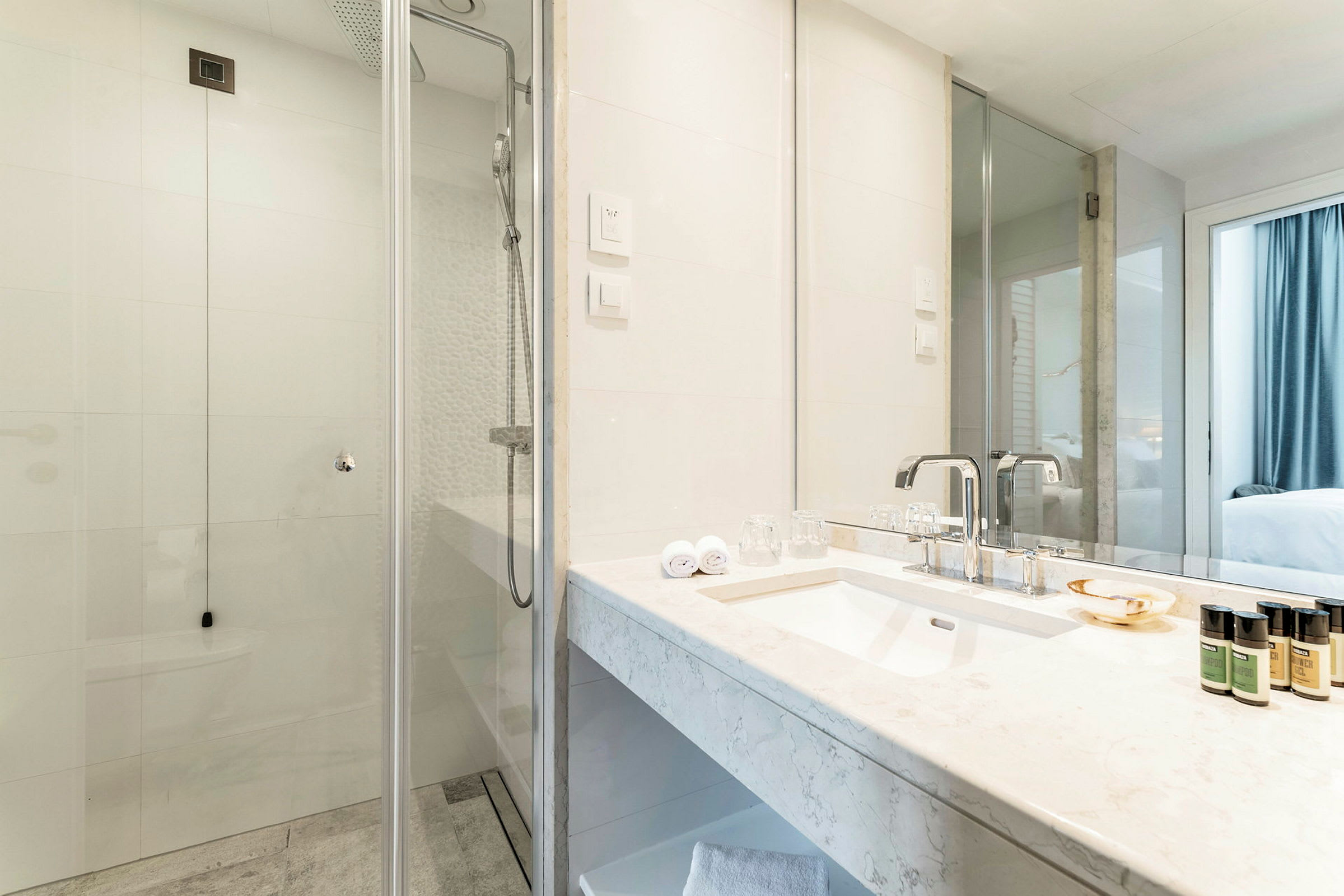 Et moderne badeværelse med en glasbruser, en marmoreret håndvask og toiletartikler i små flasker. (AI-genereret tekst)