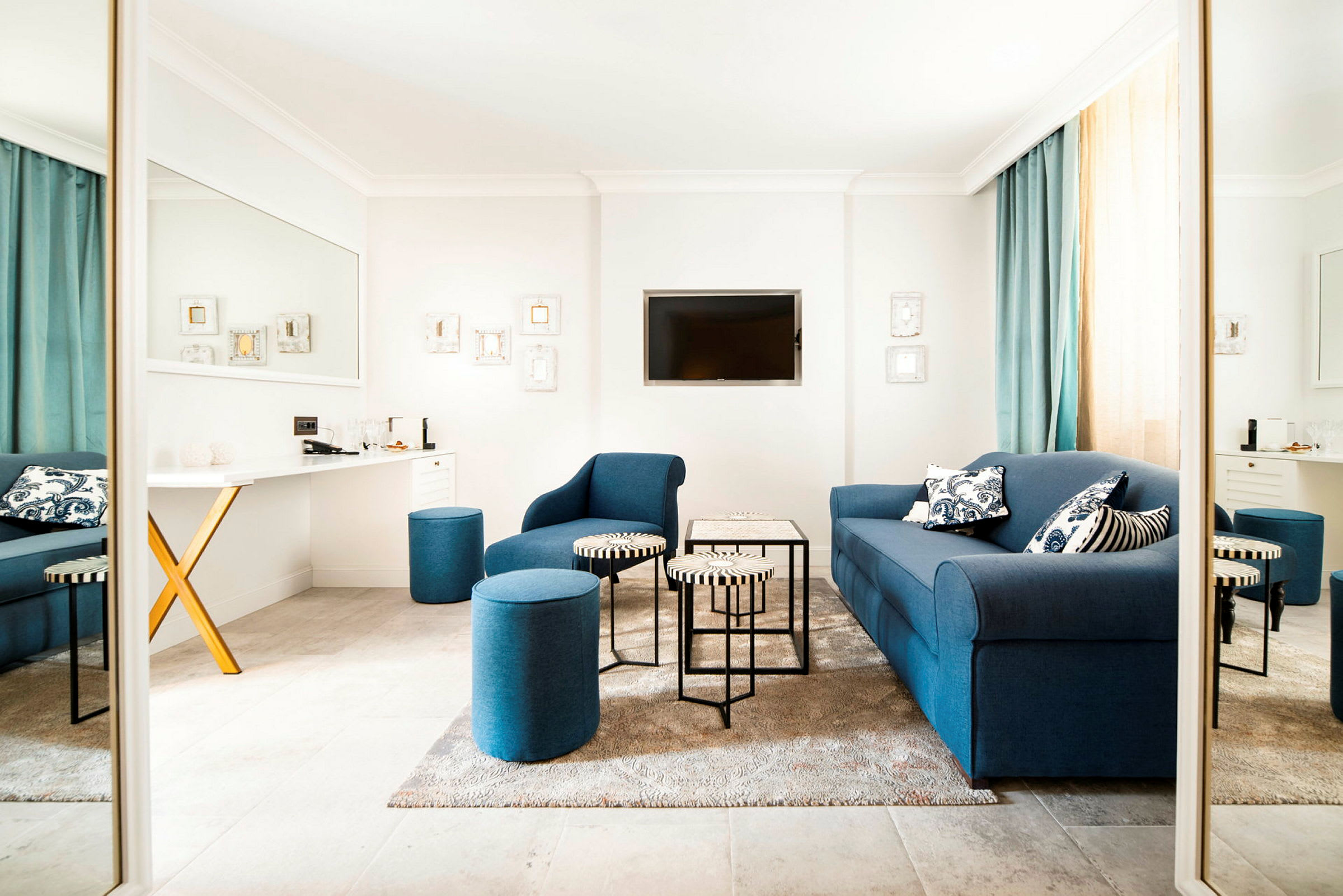 En moderne indrettet stue med blå sofaer og siddepuffer, et lille bord og et vægmonteret TV. (AI-genereret tekst)
