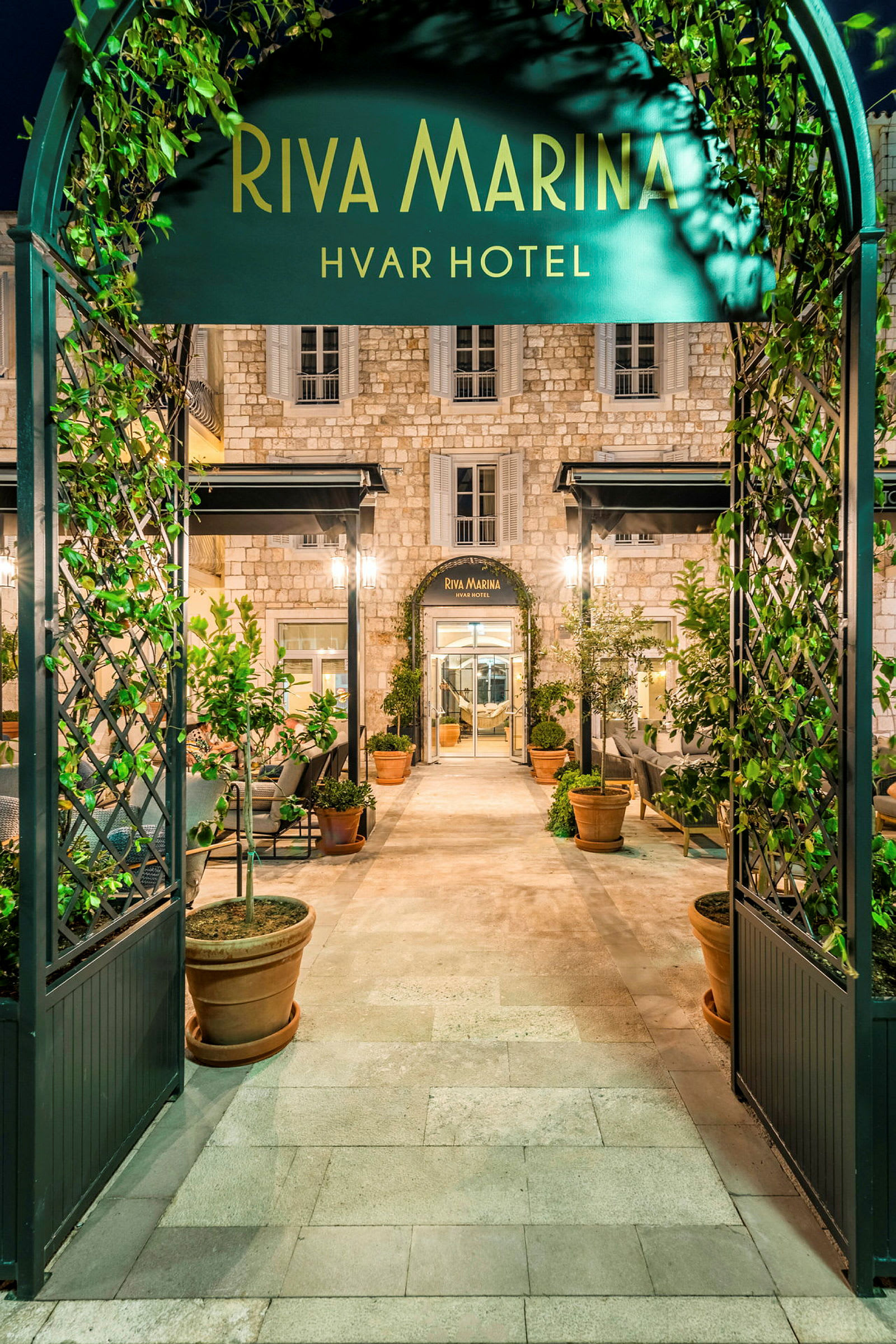 Indgang til Riva Marina Hvar Hotel med frodige planter og elegant arkitektur. (AI-genereret tekst)