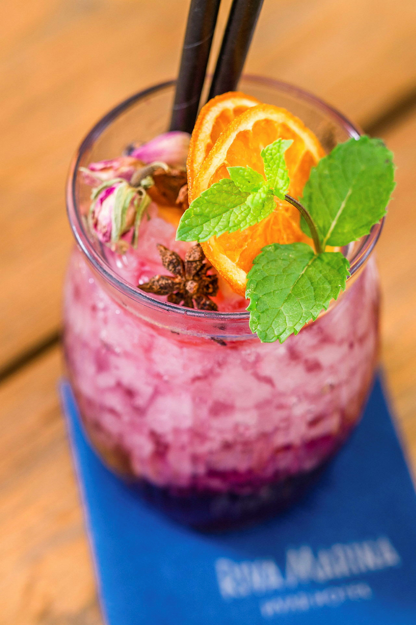 Et glas med rosa knust is og dekorationer af appelsinskiver, mynte og krydderier. (AI-genereret tekst)