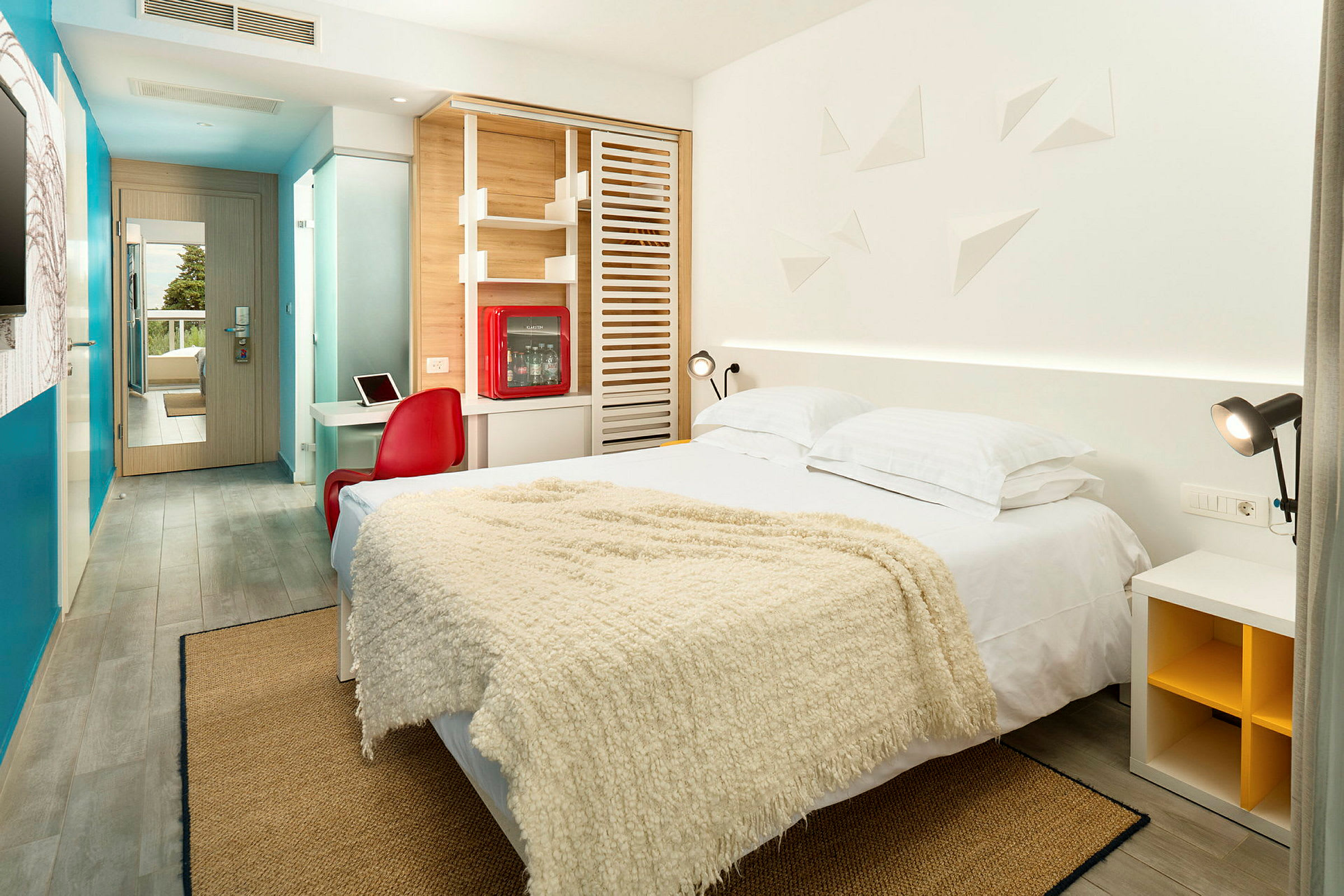 Et moderne indrettet hotelværelse med en dobbeltseng, farverige dekorationer og et skrivebord. (AI-genereret tekst)