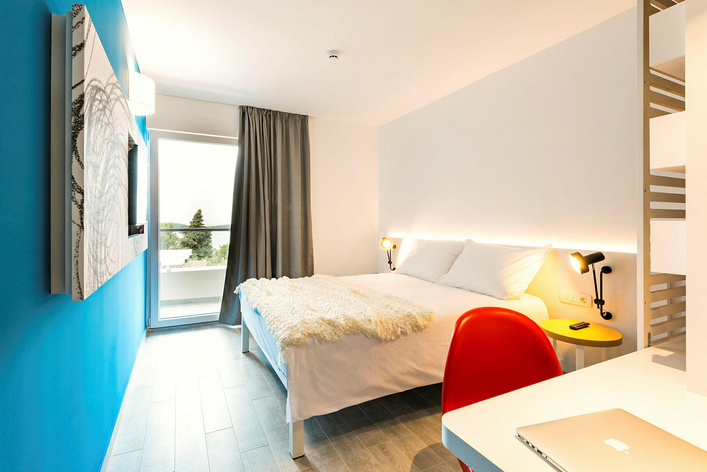Moderne indrettet hotelværelse med en dobbeltseng, skrivebord og en blå væg. (AI-genereret tekst)