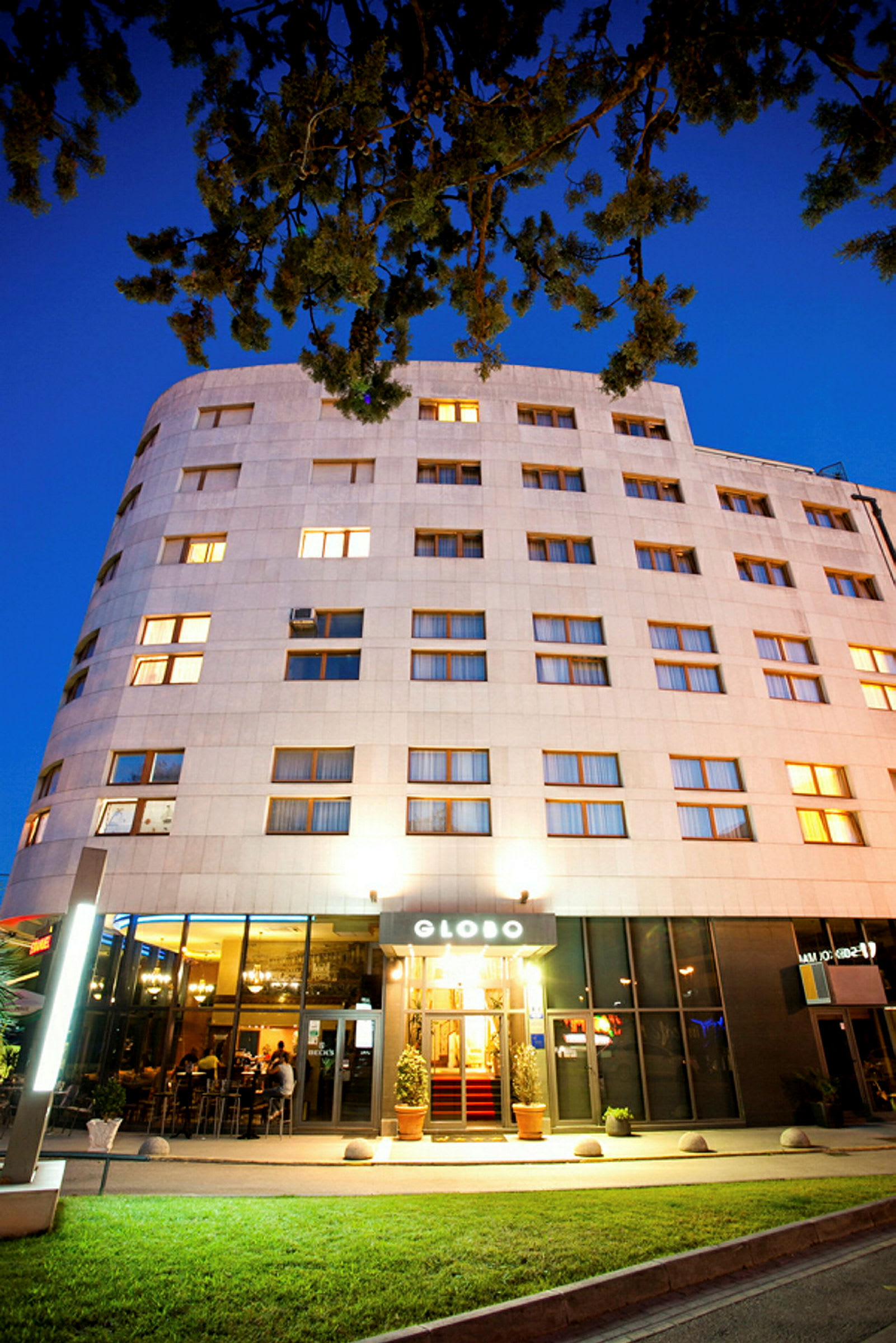 Et hotel med oplyst facade og indgang, fotograferet i skumringen. (AI-genereret tekst)