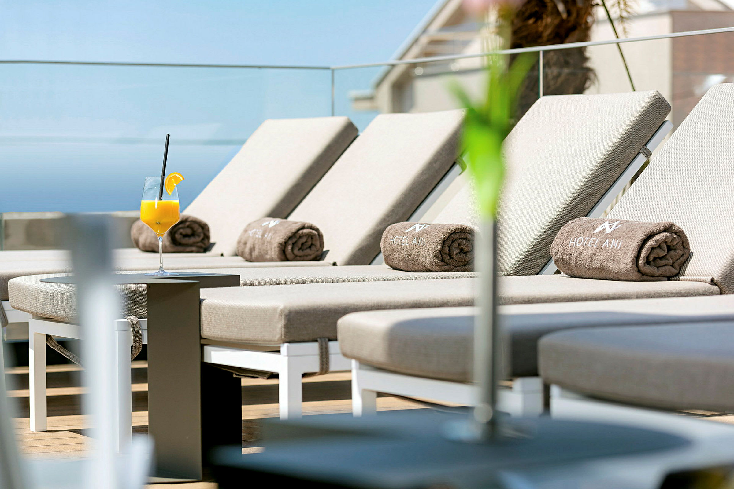 Liggestole med hotelhåndklæder på en terrasse, et glas appelsinjuice står på et bord. (AI-genereret tekst)