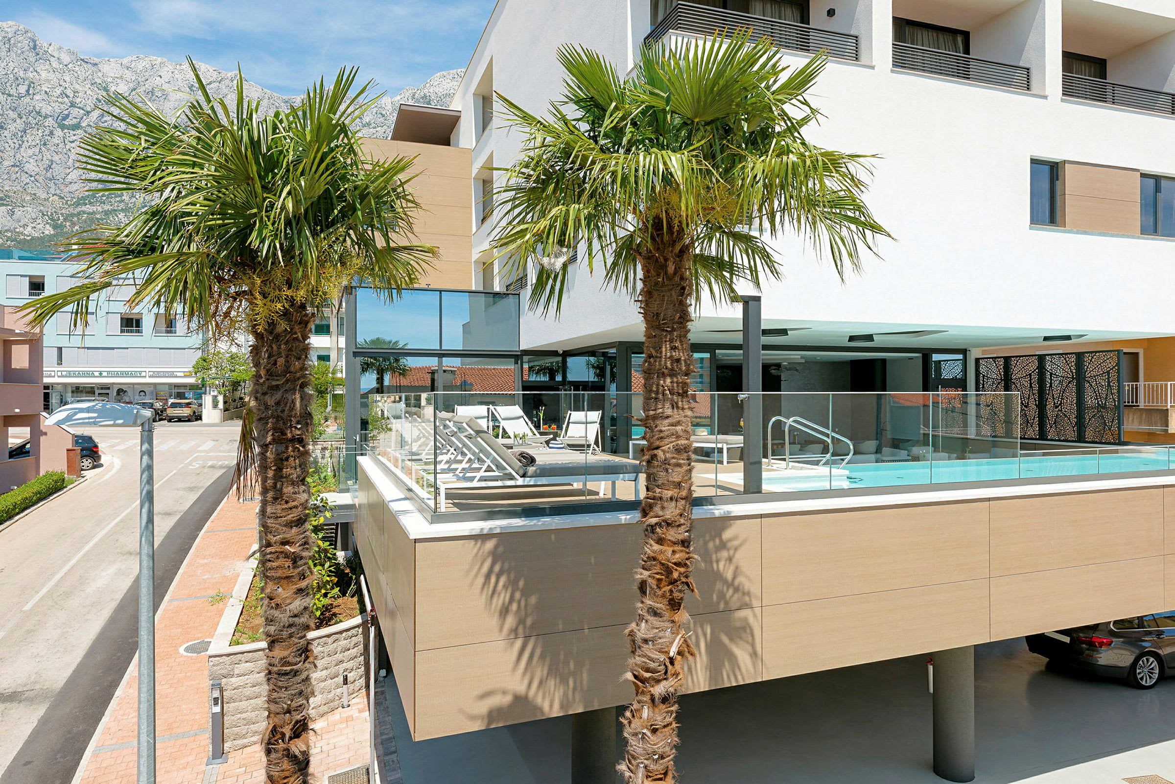 Udendørs billede af et moderne hotel med pool og liggestole, omgivet af palmer. (AI-genereret tekst)