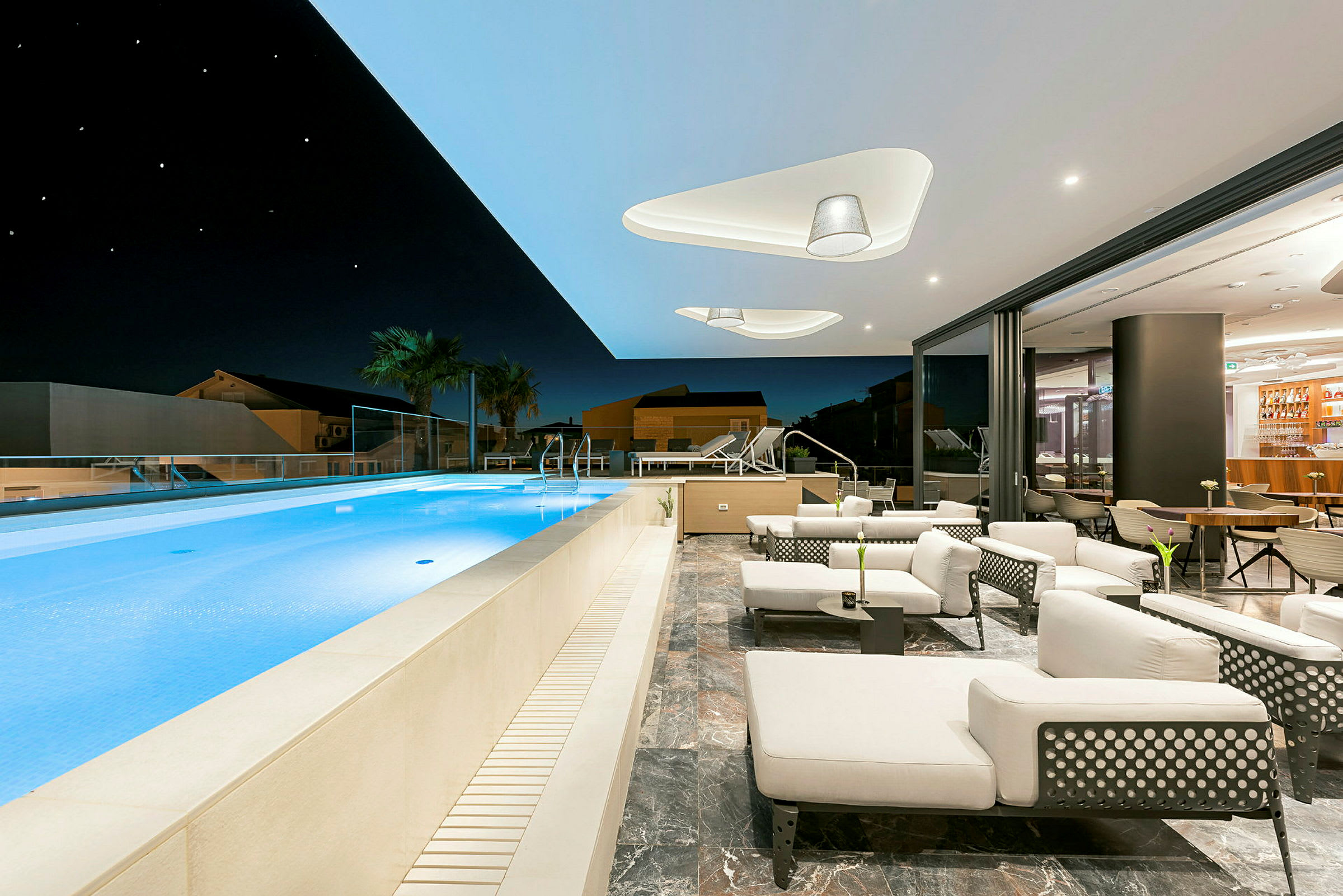 En moderne terrasse med udendørs pool, liggestole og siddepladser under nattehimlen. (AI-genereret tekst)