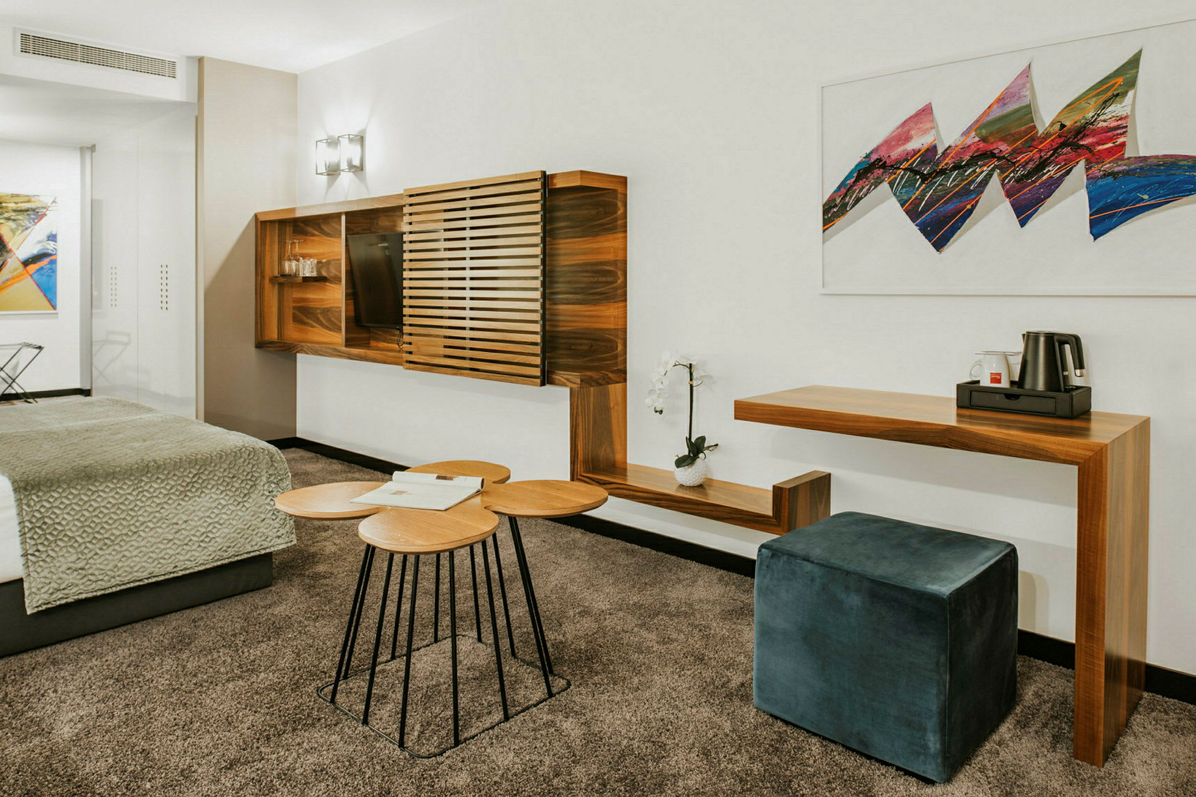 Et moderne hotelværelse med træmøbler, en siddepuf og kunst på væggen. (AI-genereret tekst)