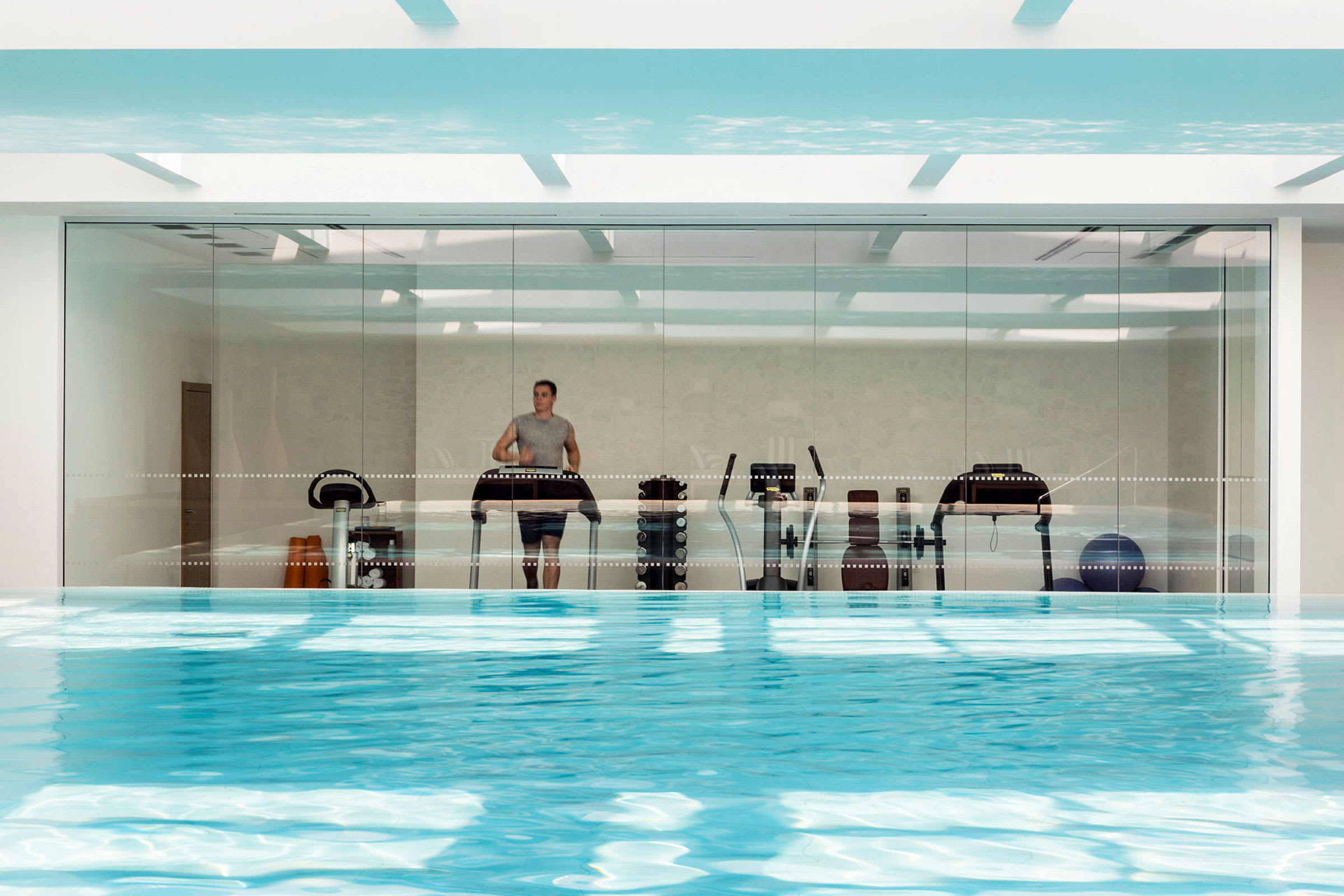 En indendørs pool med udsigt til en glasvæg, som viser træningsudstyr. (AI-genereret tekst)