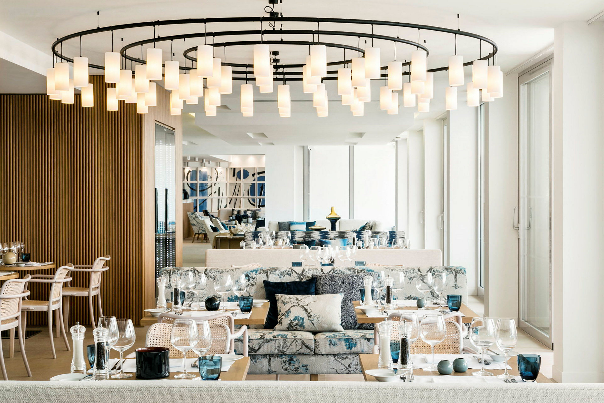 Interiør af en elegant restaurant med dækkede borde, moderne stole og en hængende lysekrone i loftet. (AI-genereret tekst)