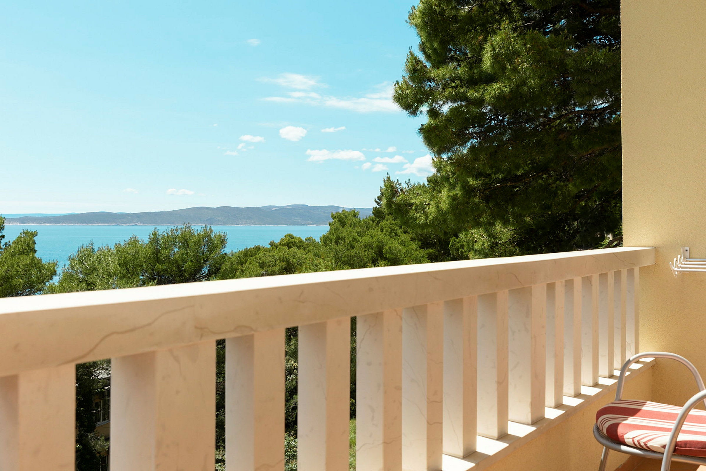 En balkon med udsigt over havet og træer. (AI-genereret tekst)