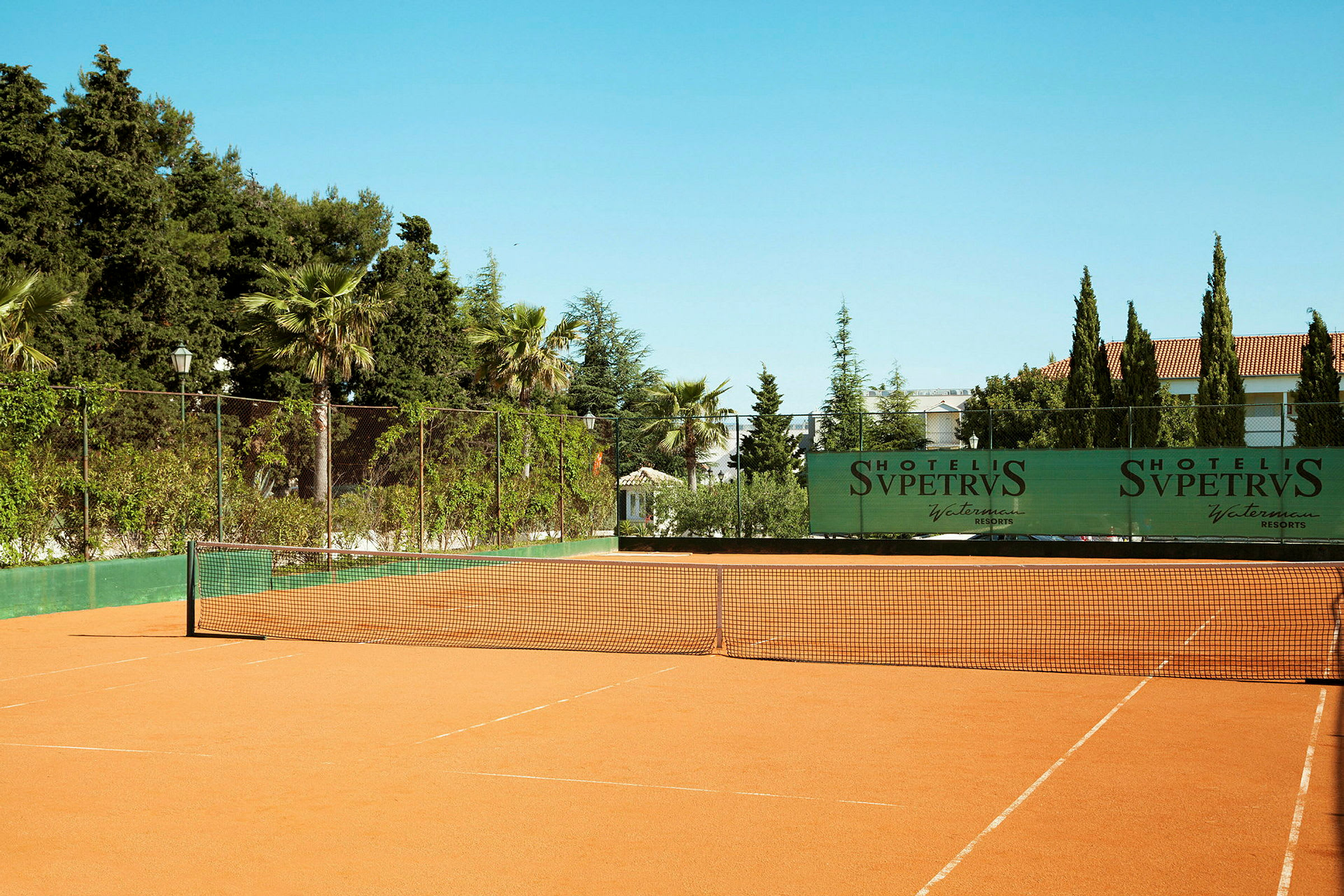 Tennisbane med omkringliggende træer og buske. (AI-genereret tekst)