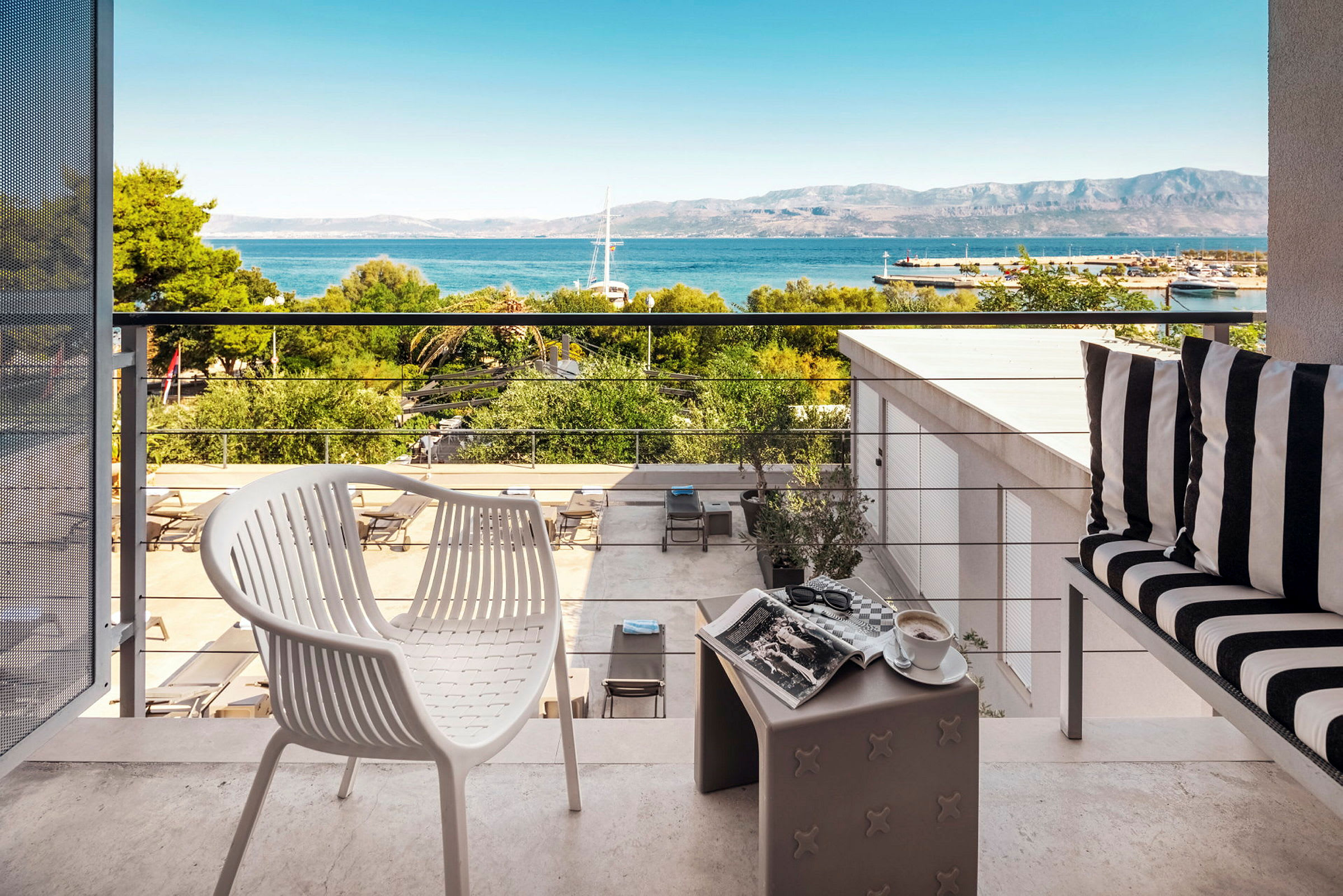 Udsigt fra en terrasse med møbler, med udsigt til havet og bjergene. (AI-genereret tekst)