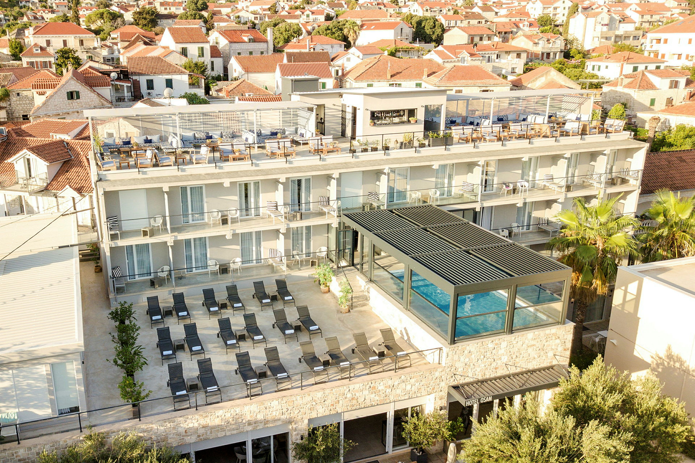 Udsigt over hotel med pool, solsenge og tagterrasse i bymiljø. (AI-genereret tekst)