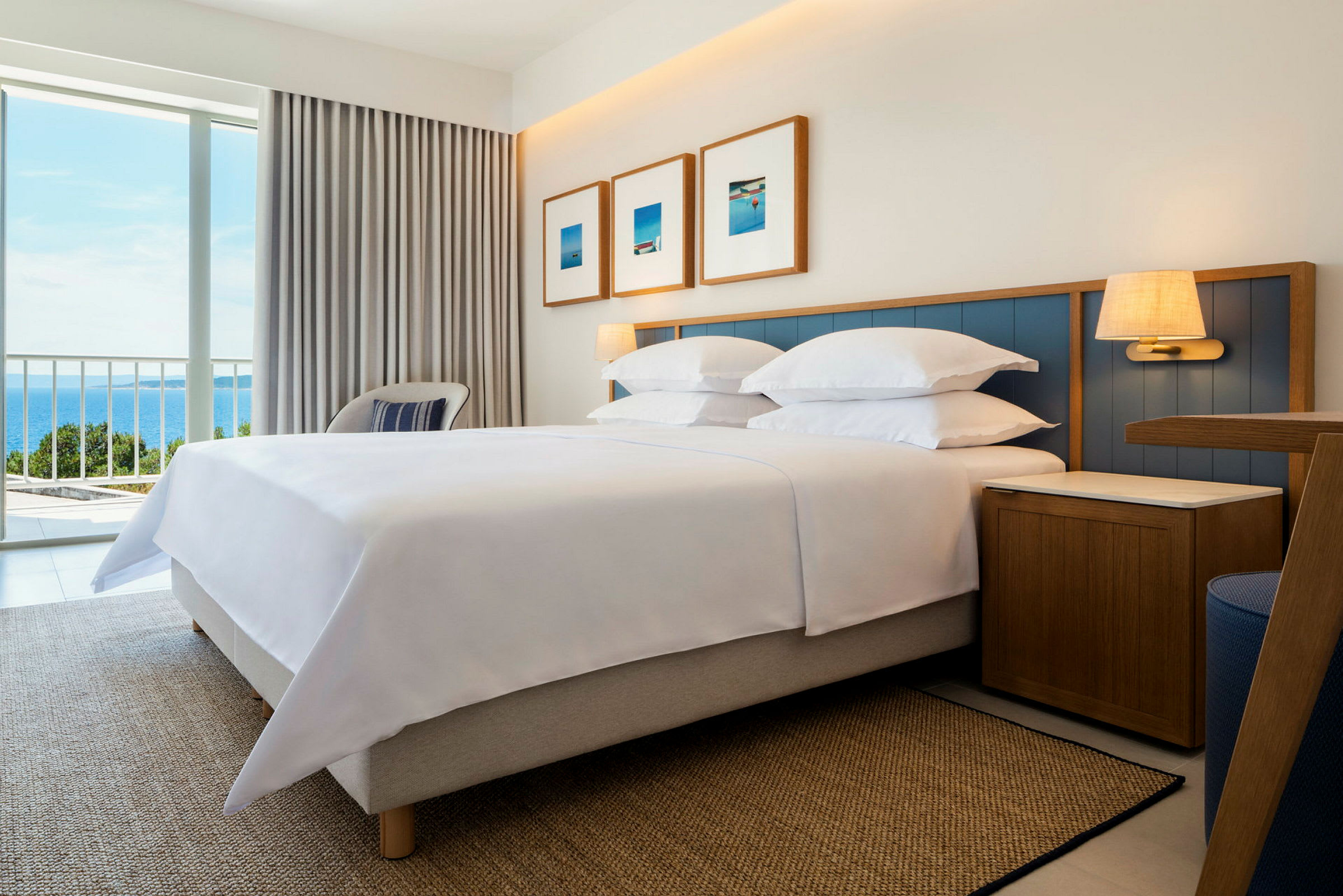 Hotelværelse med seng, natbord og vindue med udsigt til havet. (AI-genereret tekst)