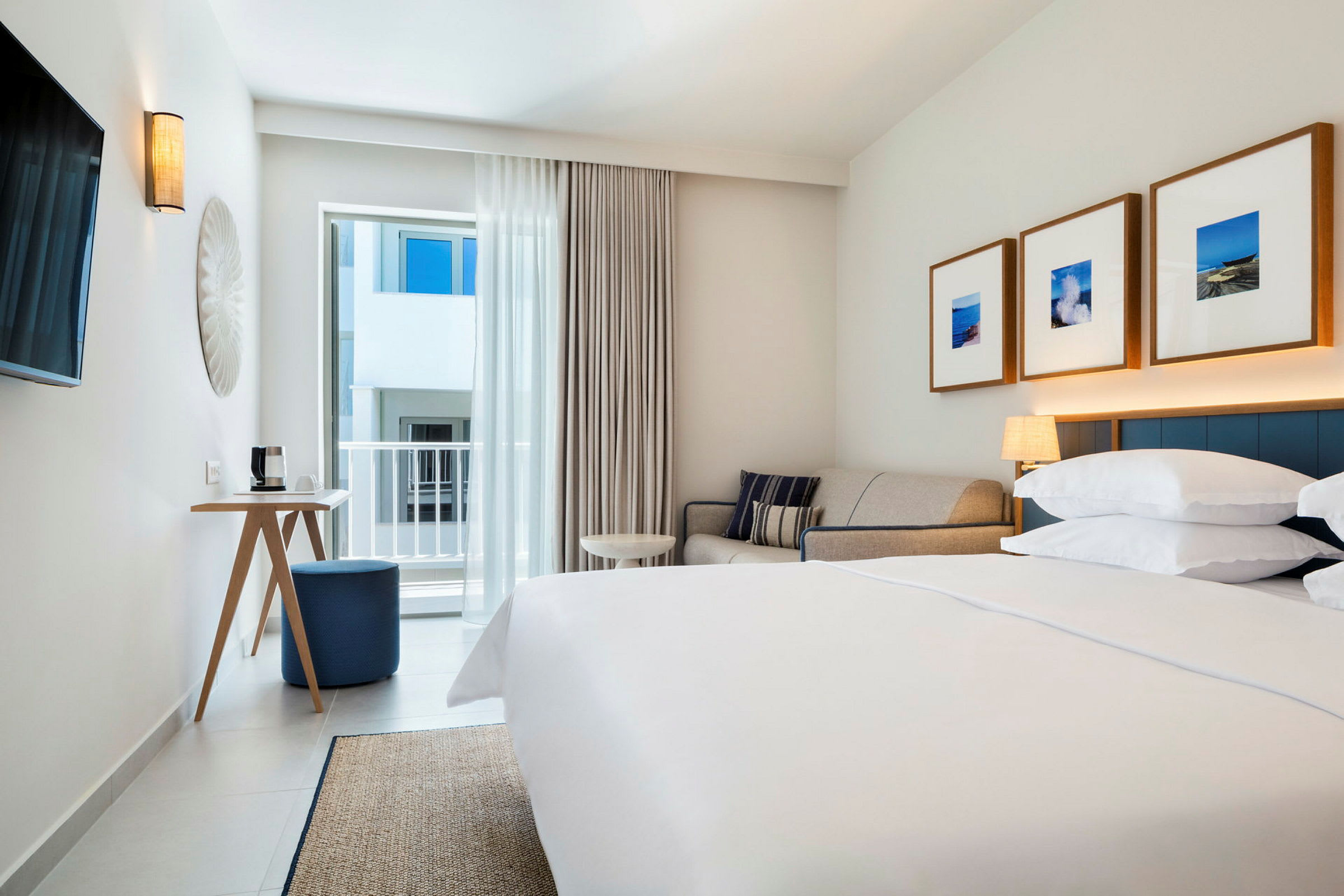 Moderne hotelværelse med dobbeltseng, sofa og vægdekorationer, med dør der fører til altan. (AI-genereret tekst)