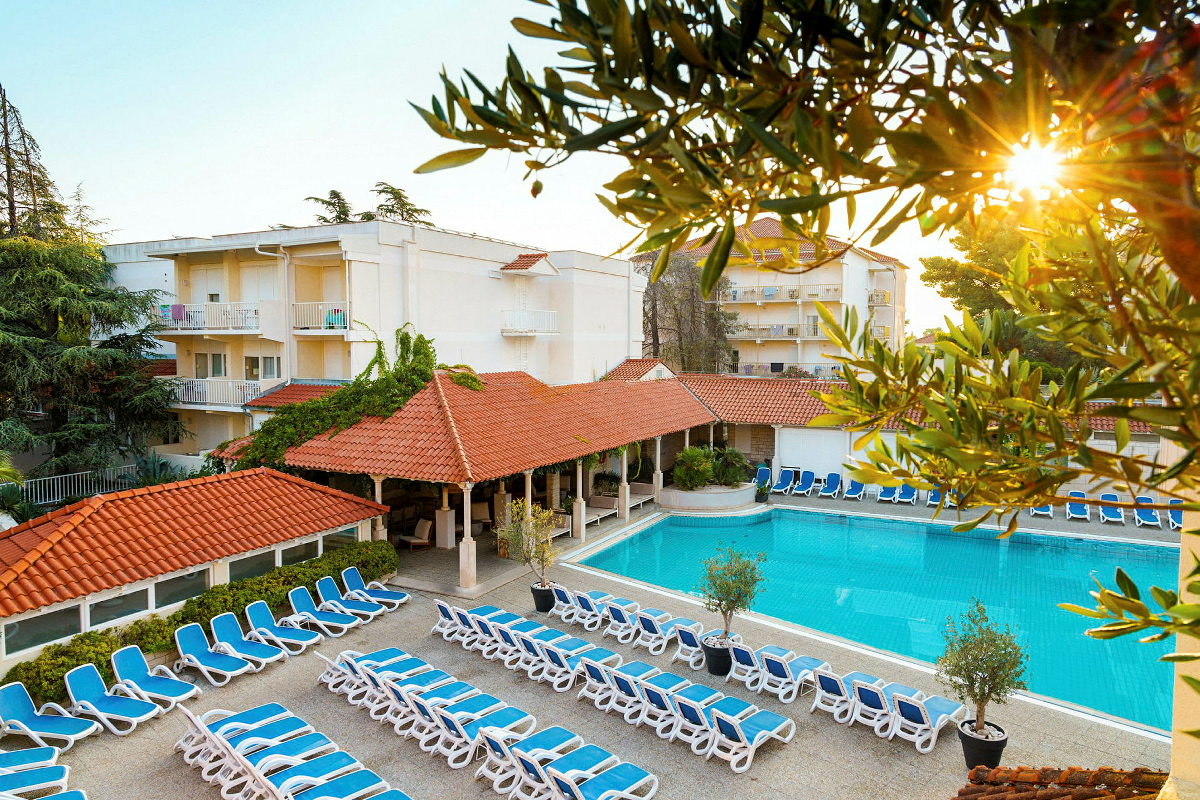 Billede af hotelområde med liggestole, pool og bygninger. (AI-genereret tekst)