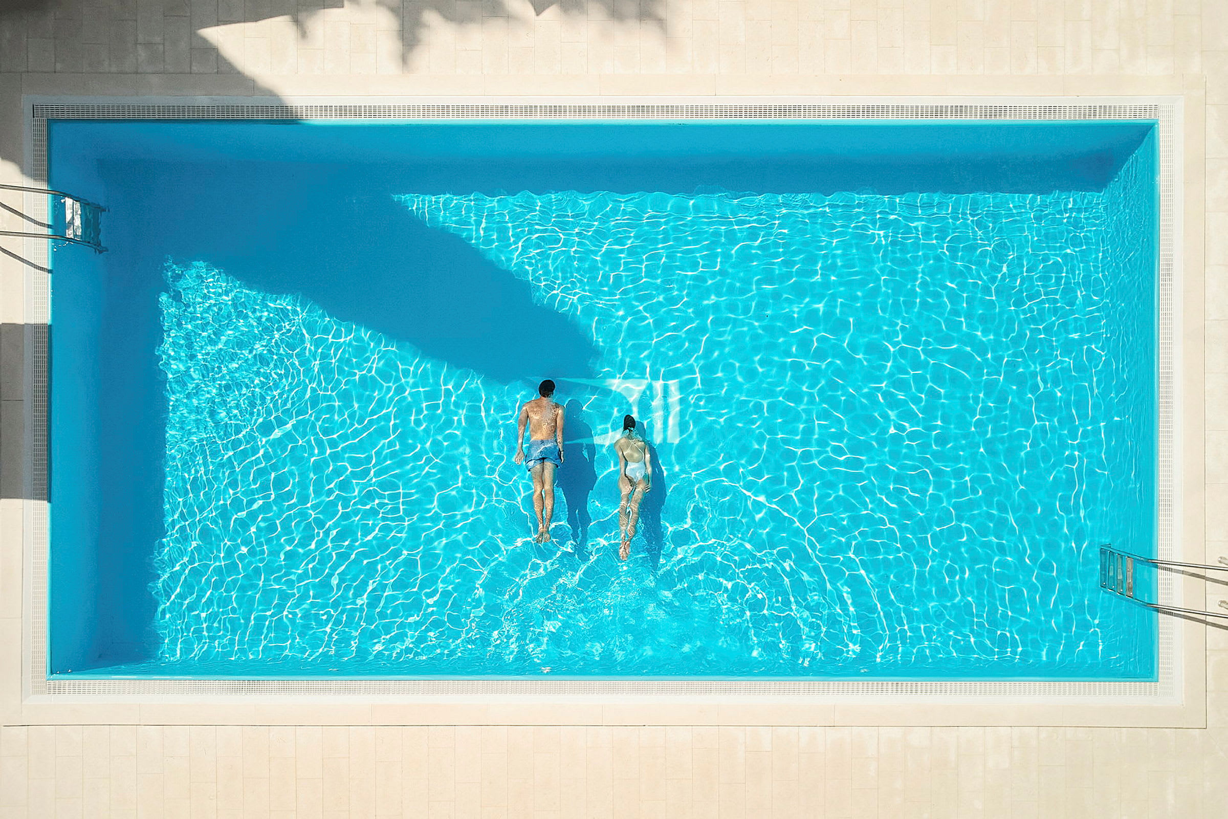 To personer svømmer i en pool set oppefra. (AI-genereret tekst)