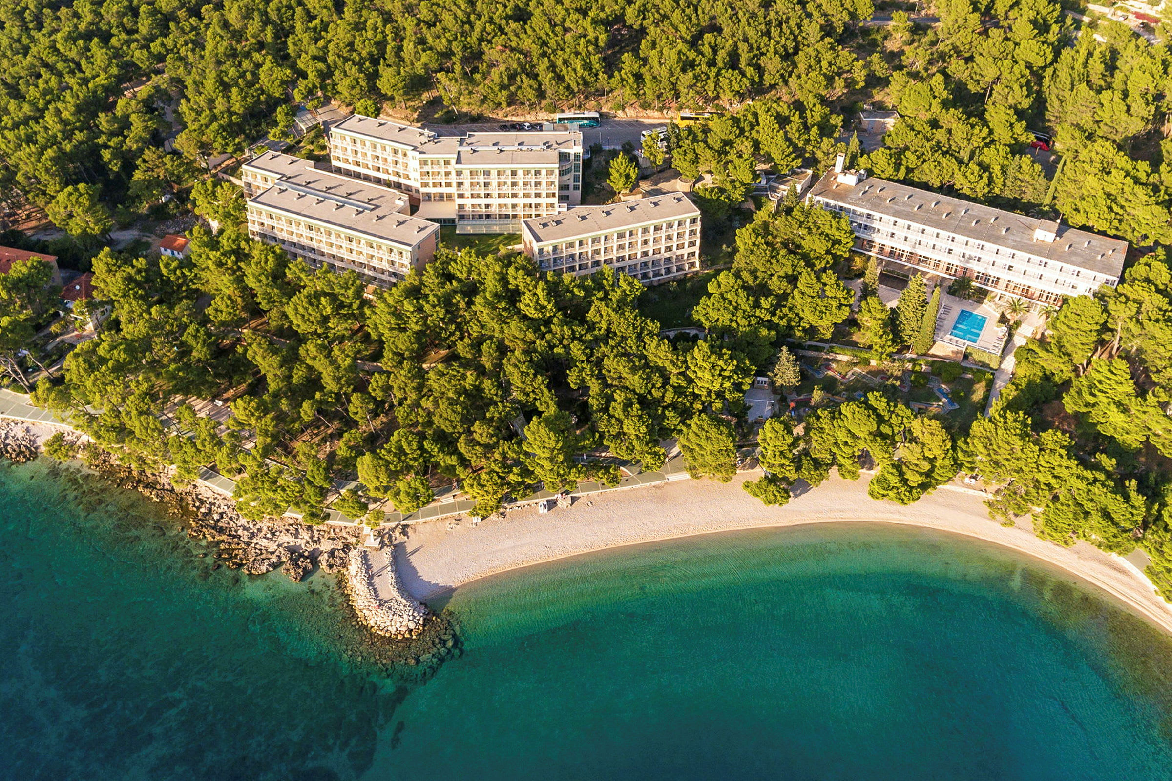 Luftfoto af hotelkompleks omgivet af skov og strand. (AI-genereret tekst)