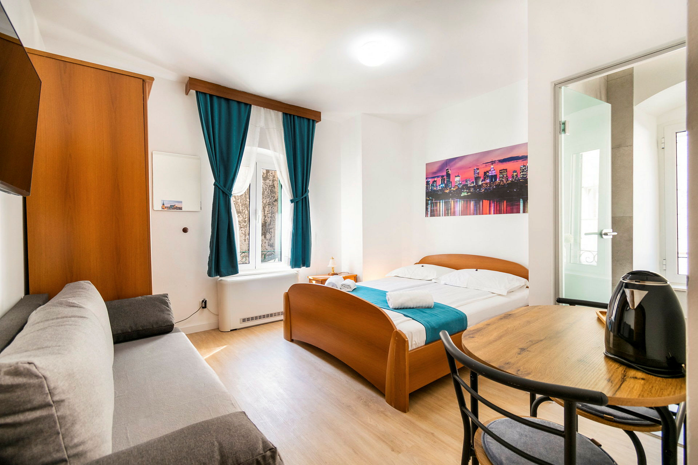 Billede af et lyst hotelværelse med en seng, sofa, bord og en elkedel. (AI-genereret tekst)