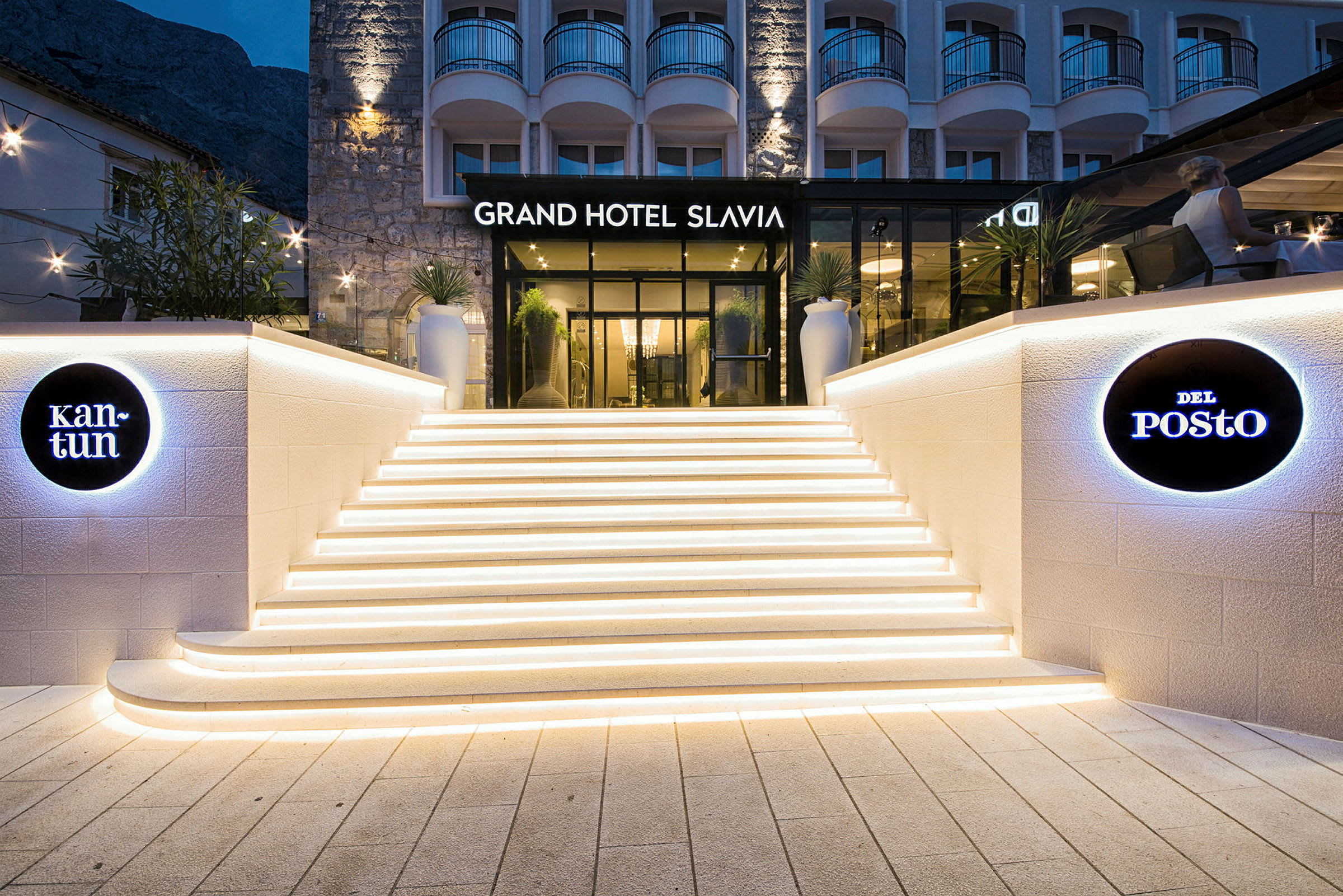 Indgang til Grand Hotel Slavia med oplyste trapper og skiltning. (AI-genereret tekst)