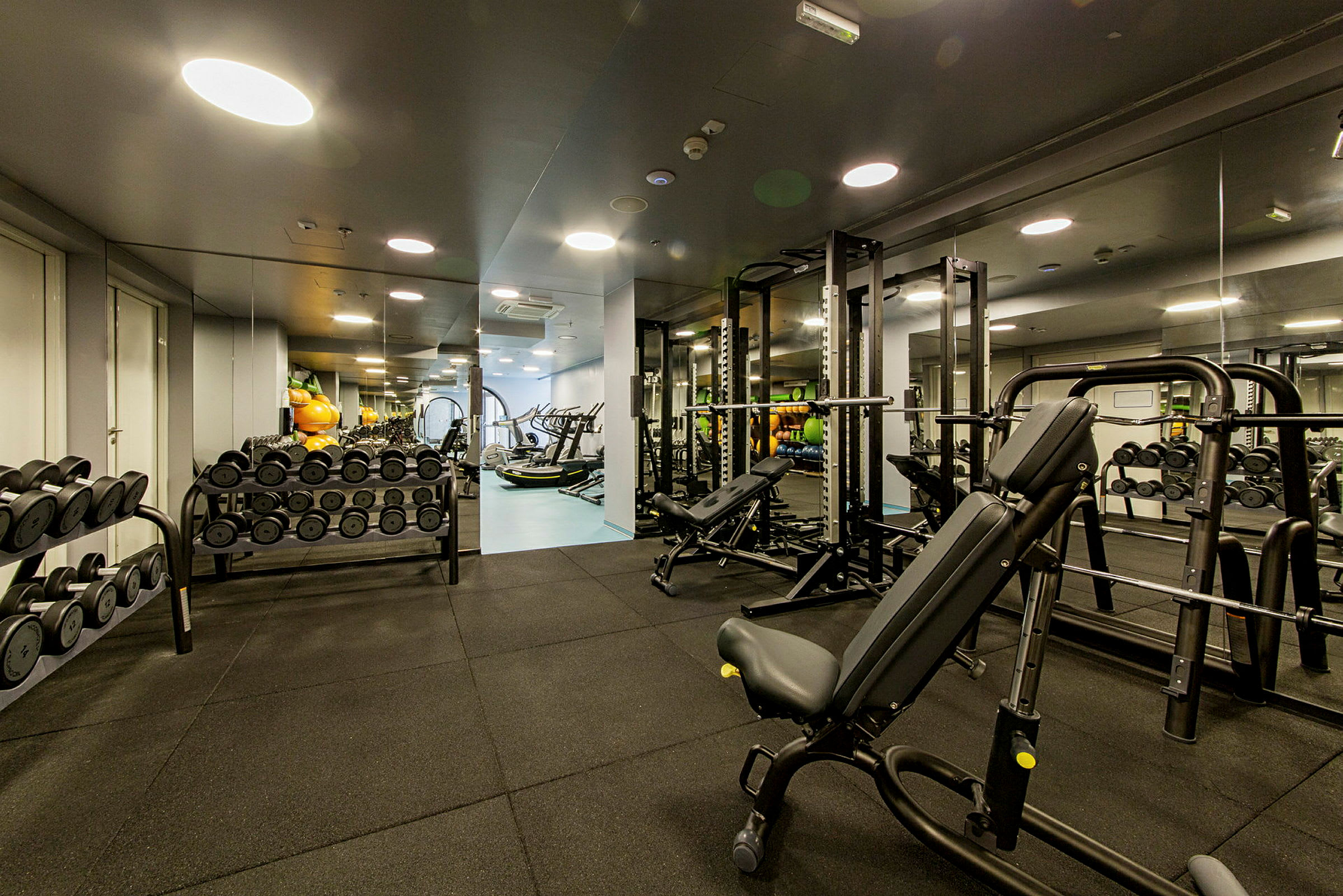 Billede af et fitnesscenter med træningsudstyr, herunder vægtskiver, håndvægte og konditionsmaskiner. (AI-genereret tekst)