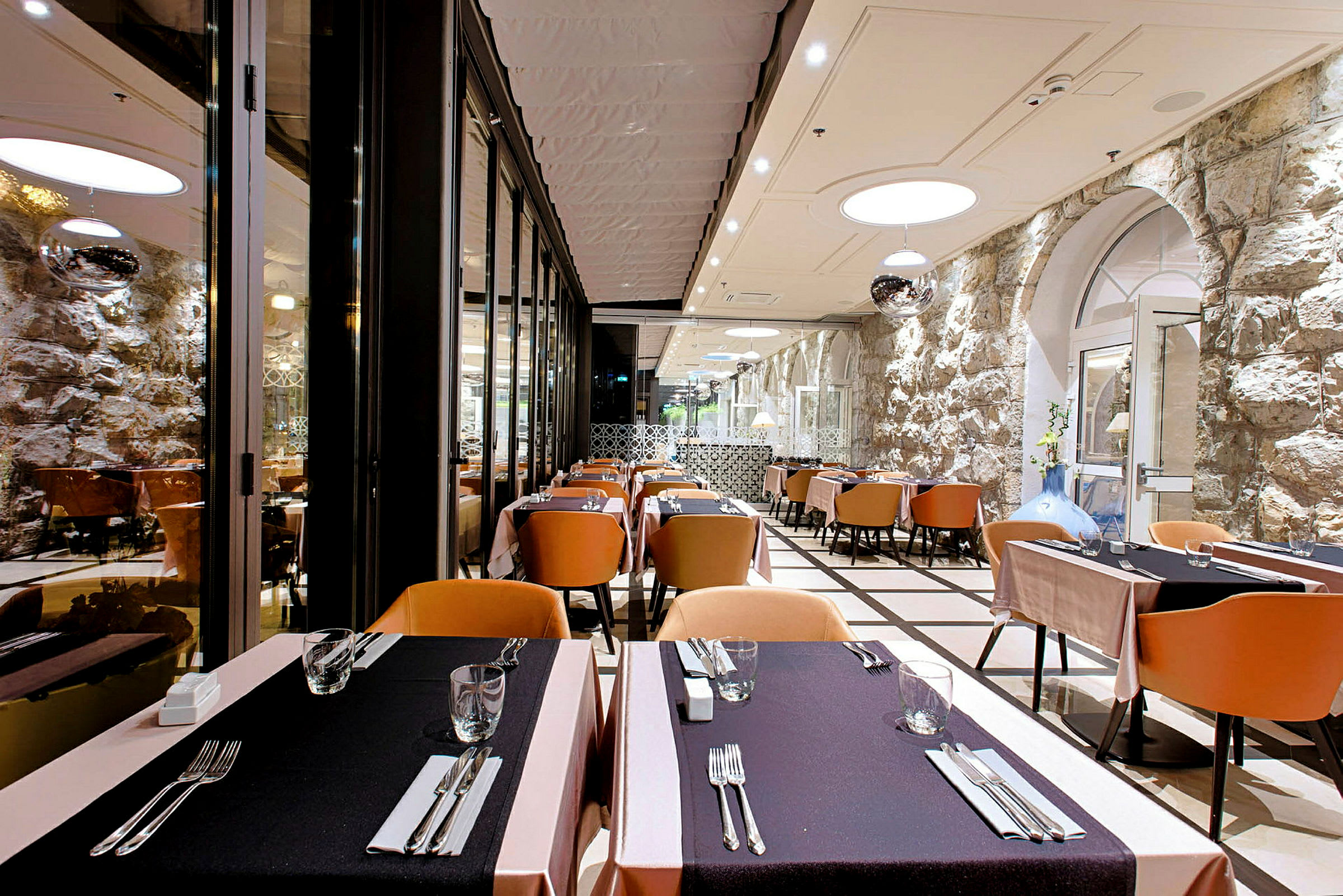 Billede af en elegant restaurant med dækkede borde og stole, stenmur i baggrunden. (AI-genereret tekst)