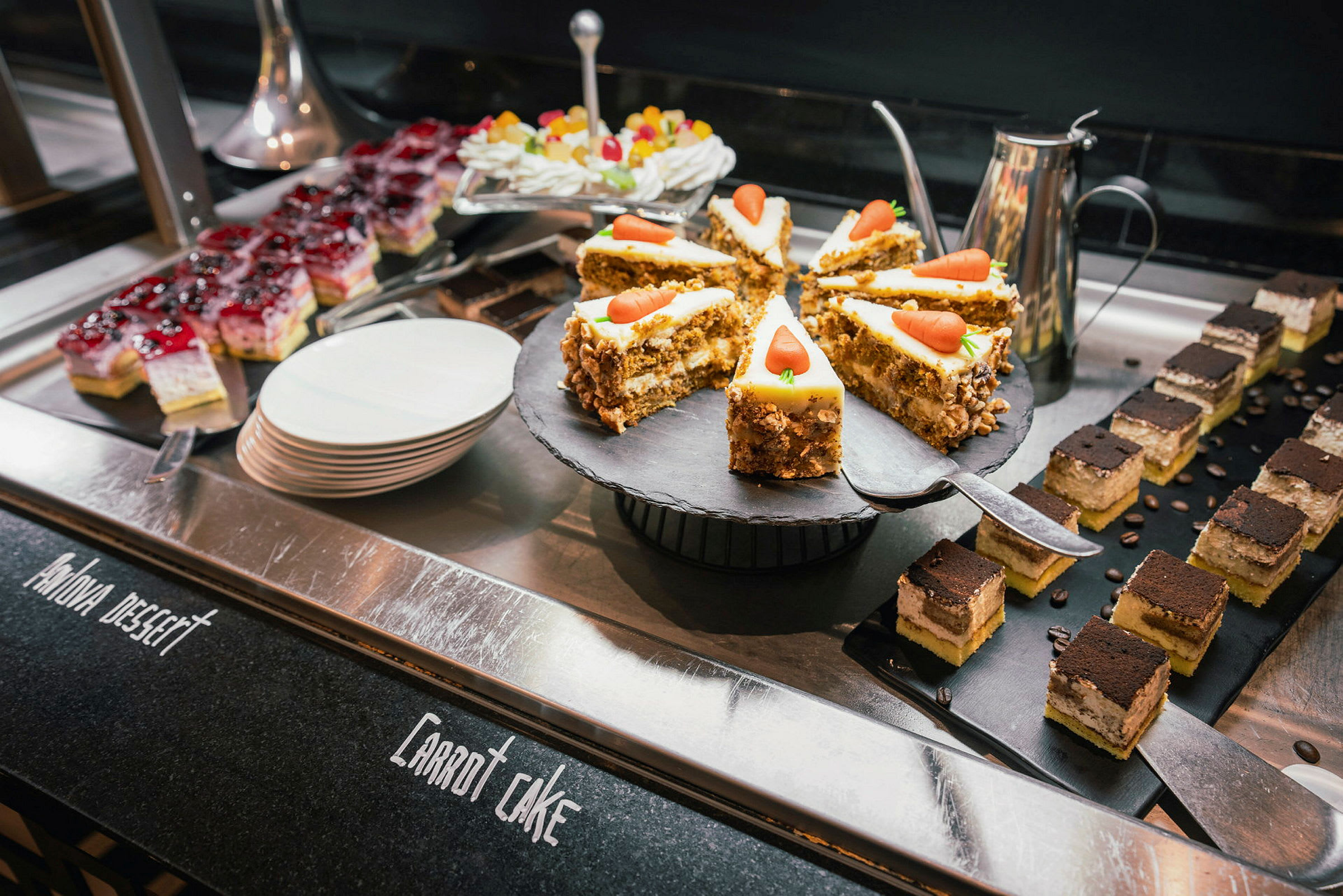 Billedet viser en buffet med forskellige desserter, inklusiv gulerodskage, små vanilje- og chokoladebøffer samt farverige vingummier. (AI-genereret tekst)