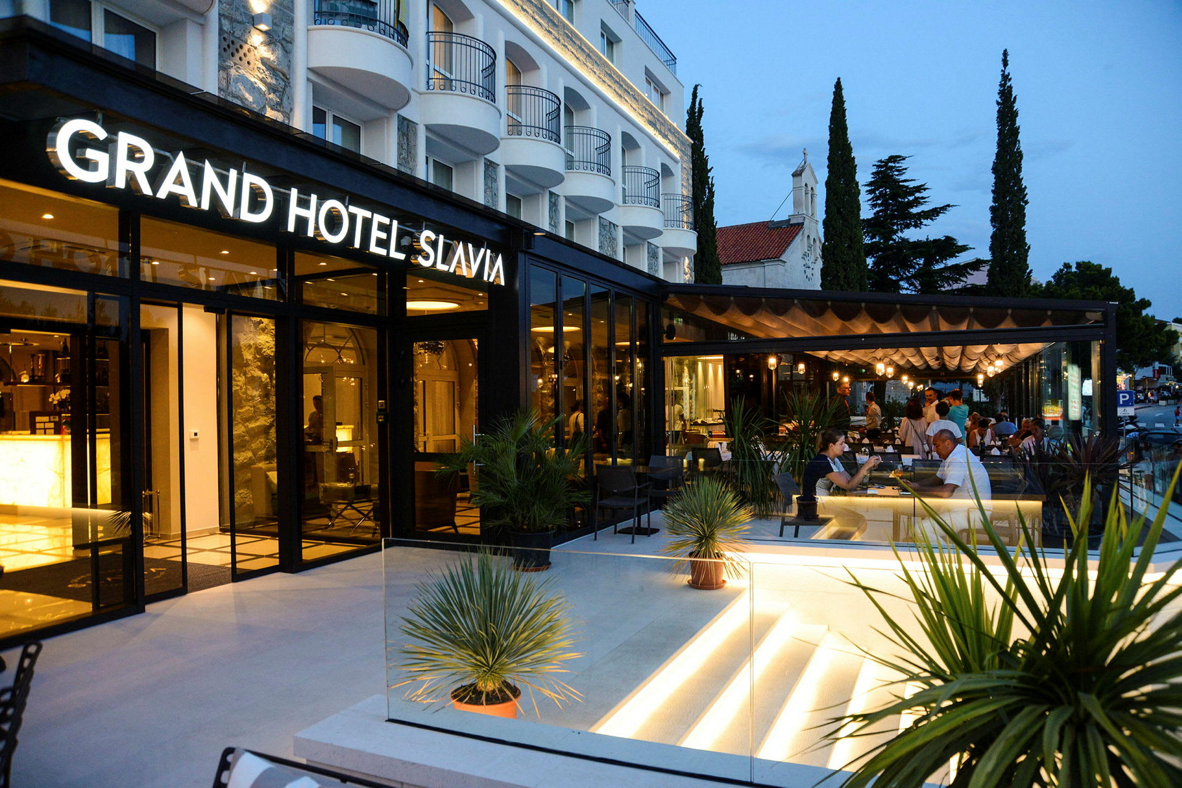 Grand Hotel Slavia med moderne udendørs servering og aftenbelysning. (AI-genereret tekst)