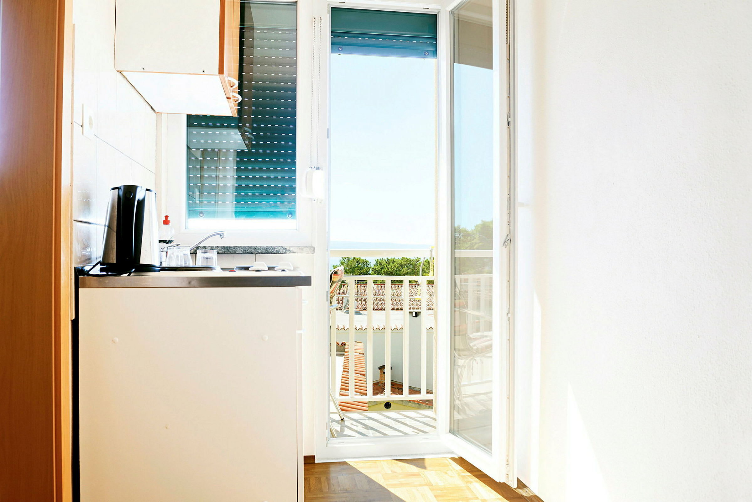 Et lille køkken med udsigt mod en balkon og havet i baggrunden. (AI-genereret tekst)