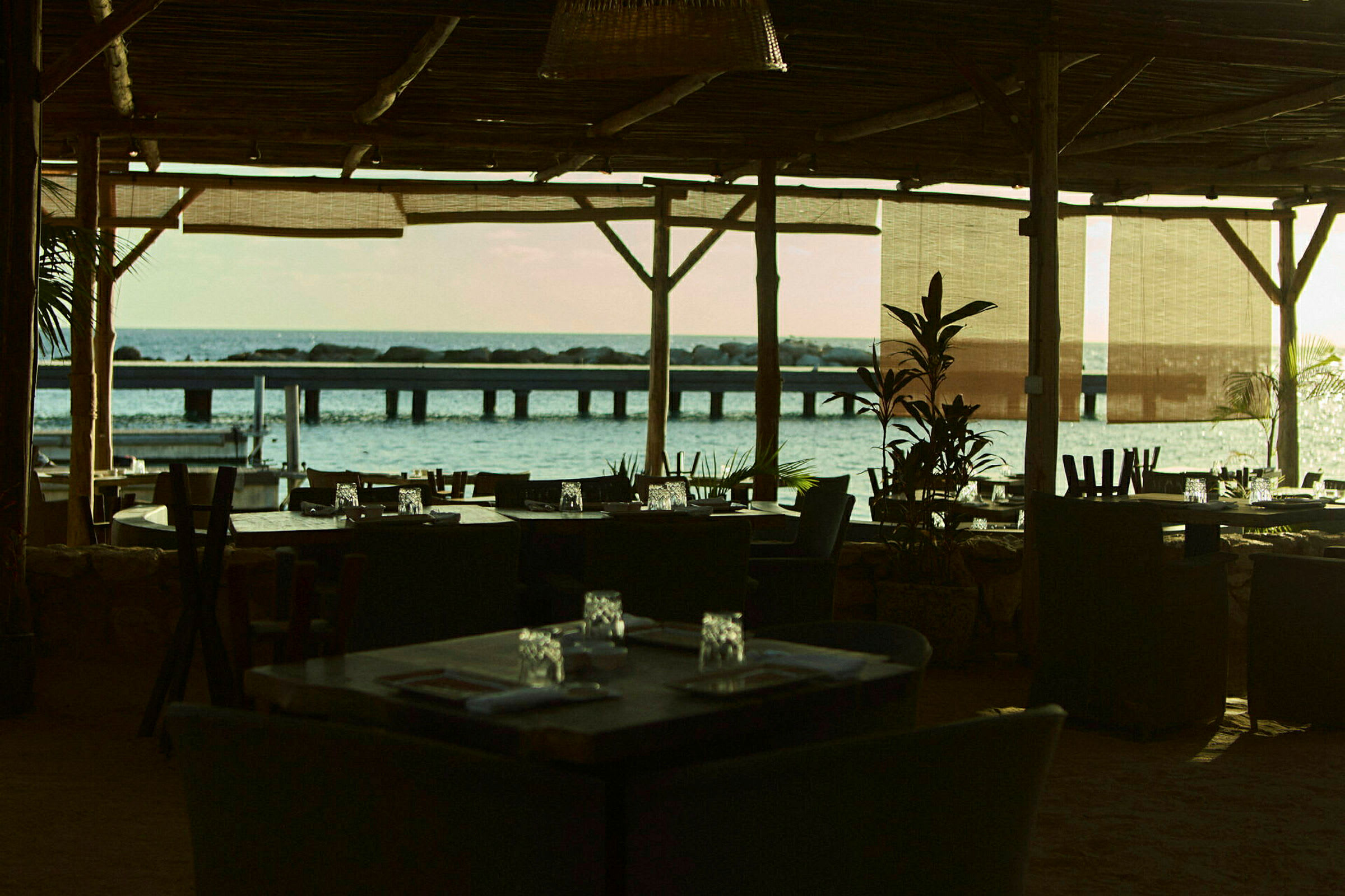 En restaurant med tag og møbler med udsigt over havet og en bro i baggrunden. (AI-genereret tekst)