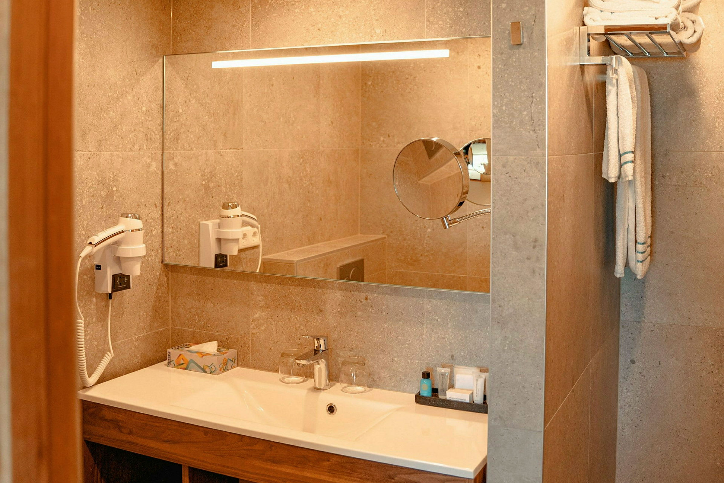 Badeværelse med spejl, håndvask og håndklædeholder. Hårtørrer og toiletsager er inkluderet. (AI-genereret tekst)