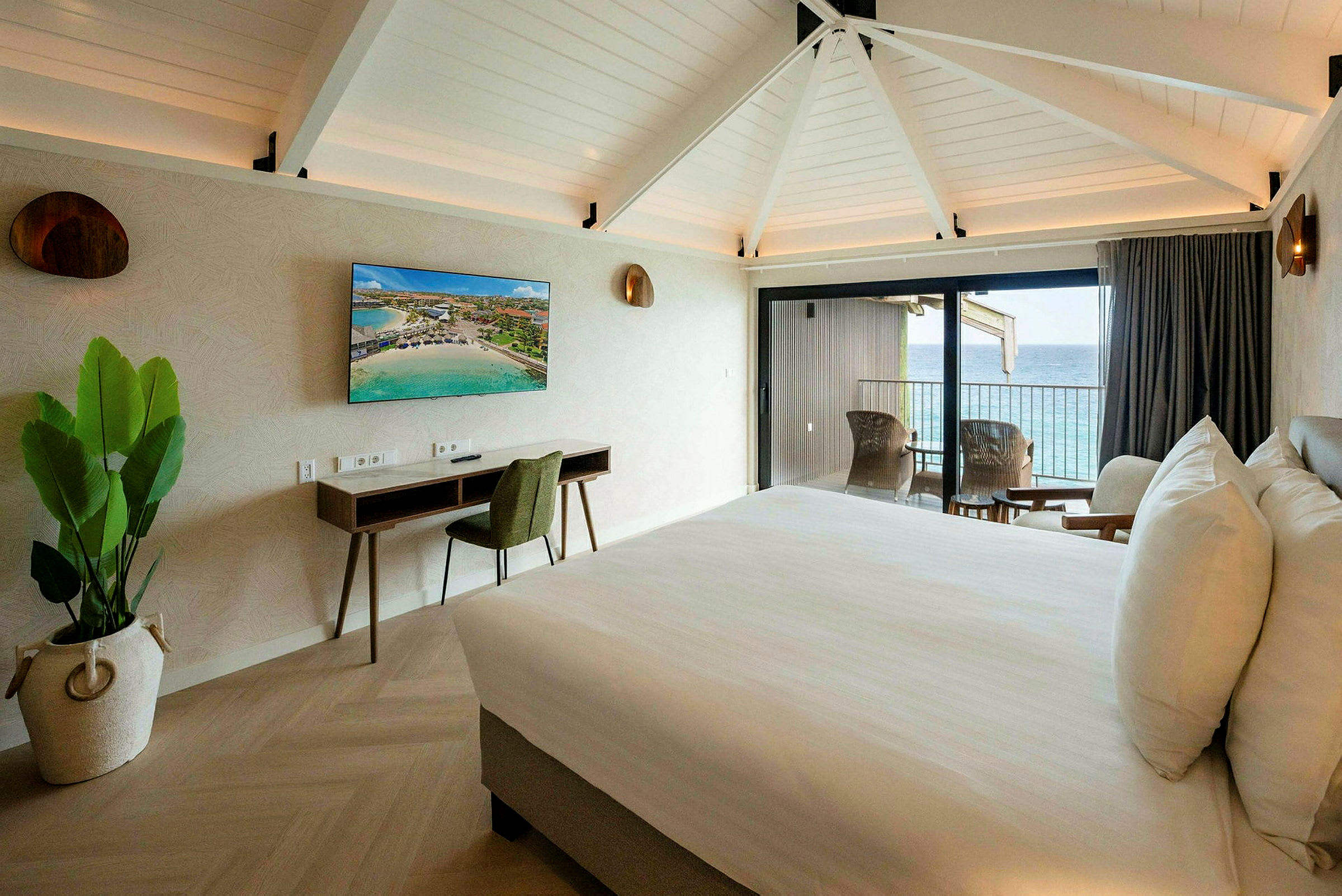 Et hotelværelse med en dobbeltseng, skrivebord, tv og balkon med udsigt over havet. (AI-genereret tekst)