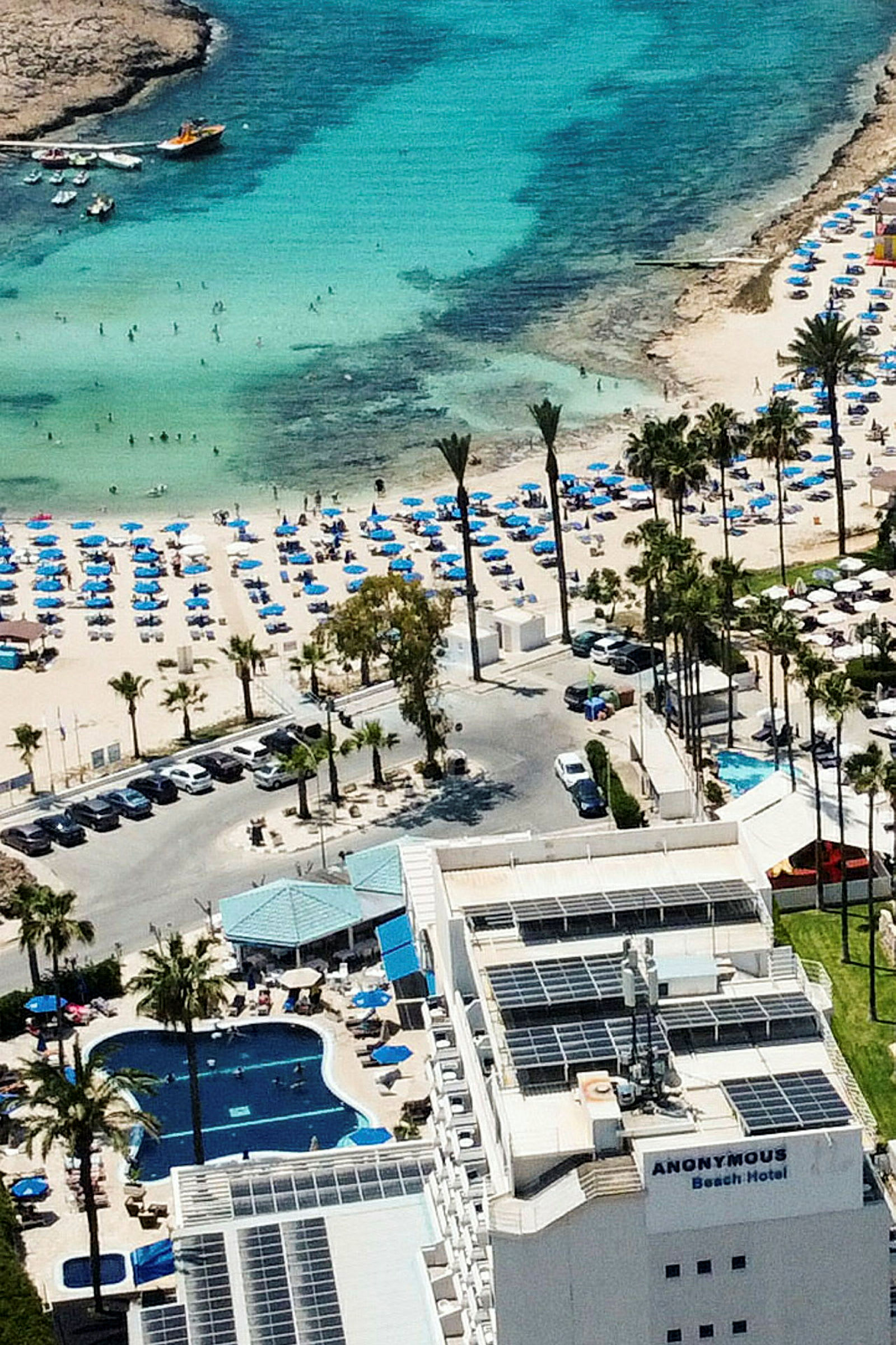 Hotel med pool og nærliggende strand fyldt med liggestole og parasoller ved et turkis hav. (AI-genereret tekst)