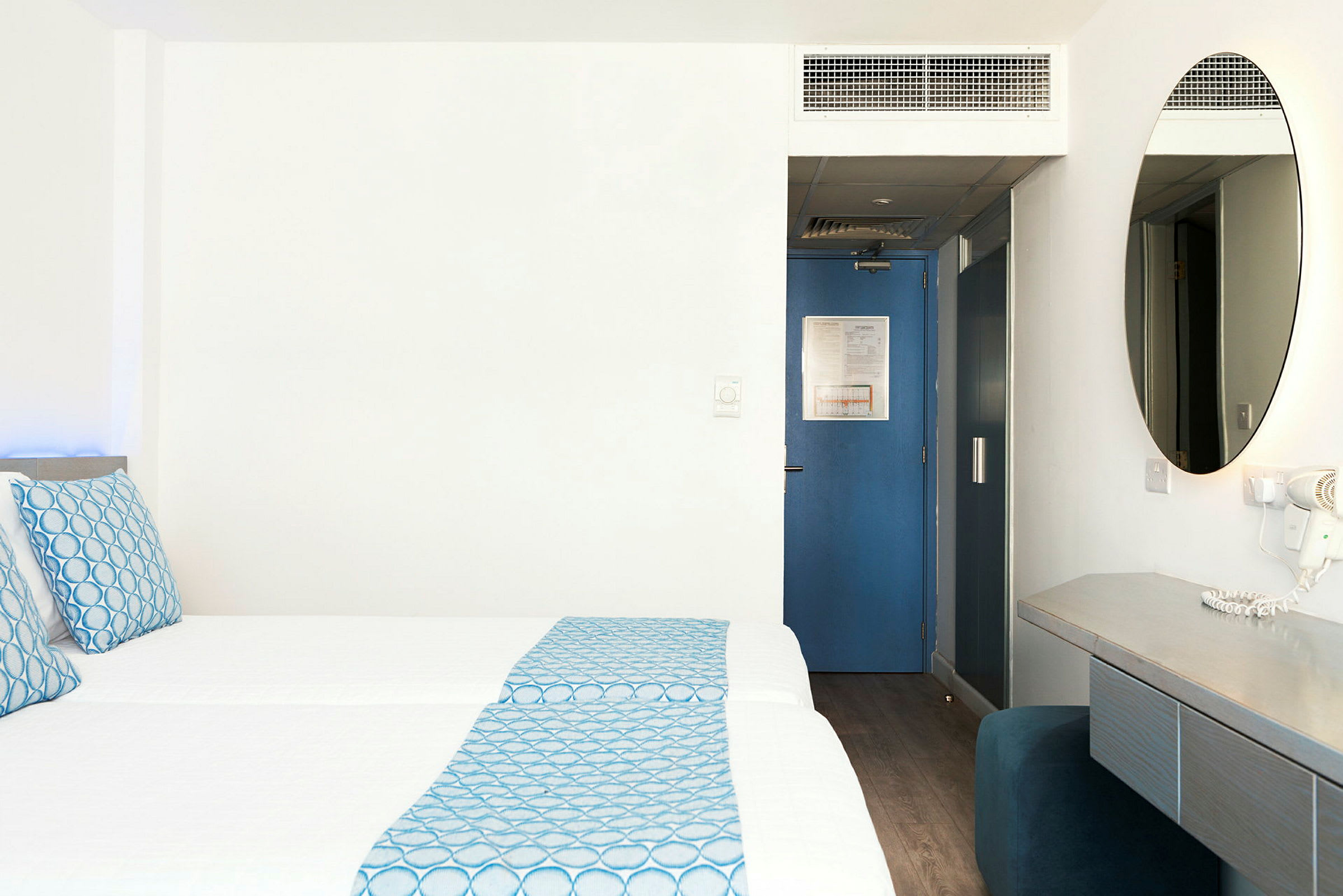 Hotelværelse med to senge, blå detaljer og skrivebord. (AI-genereret tekst)